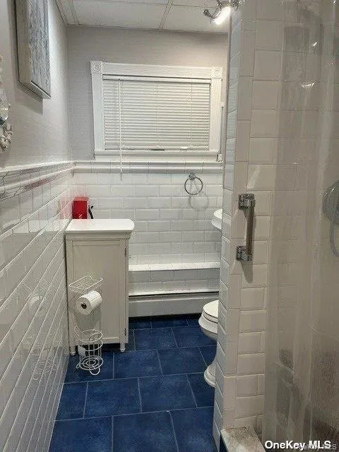 Full bath featuring a stall shower, tile walls, vanity, dark tile patterned flooring, and a wainscoted wall Full bath featuring a stall shower, tile walls, vanity, dark tile patterned flooring, and a wainscoted wall