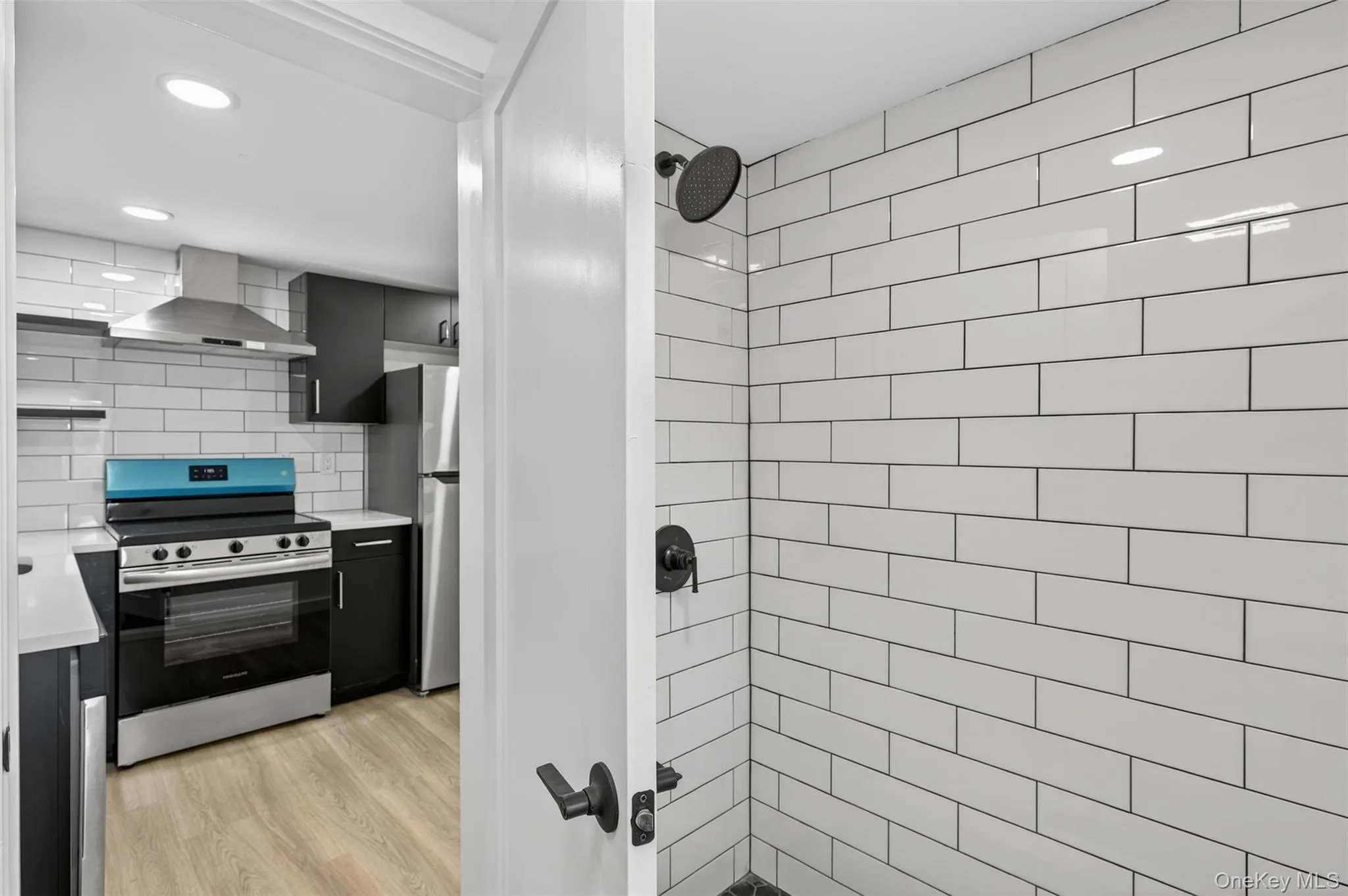 Kitchen with appliances with stainless steel finishes, light countertops, wall chimney exhaust hood, decorative backsplash, and light wood-style floors Kitchen with appliances with stainless steel finishes, light countertops, wall chimney exhaust hood, decorative backsplash, and light wood-style floors