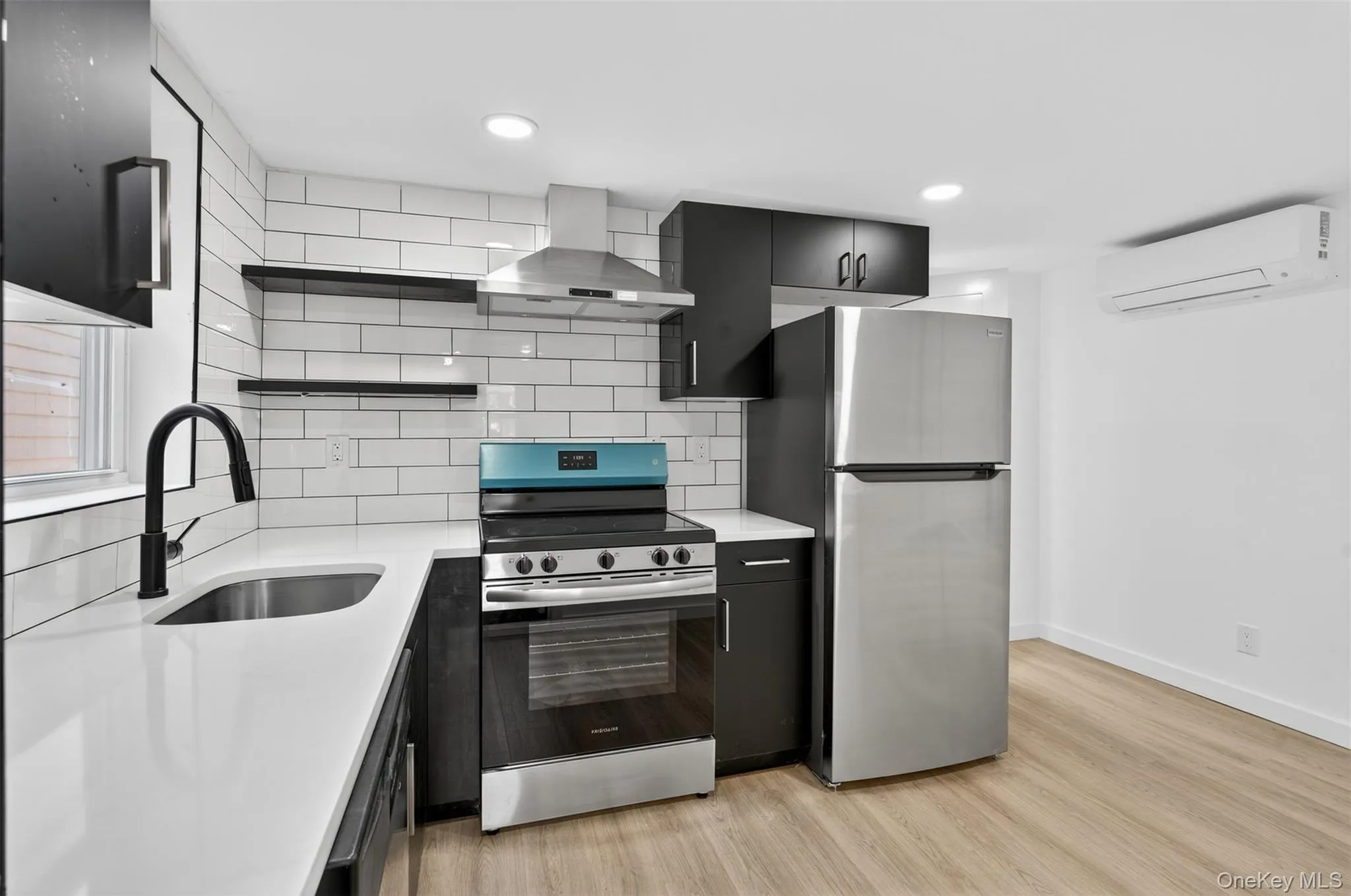 Kitchen with stainless steel appliances, open shelves, dark cabinets, island range hood, and tasteful backsplash Kitchen with stainless steel appliances, open shelves, dark cabinets, island range hood, and tasteful backsplash