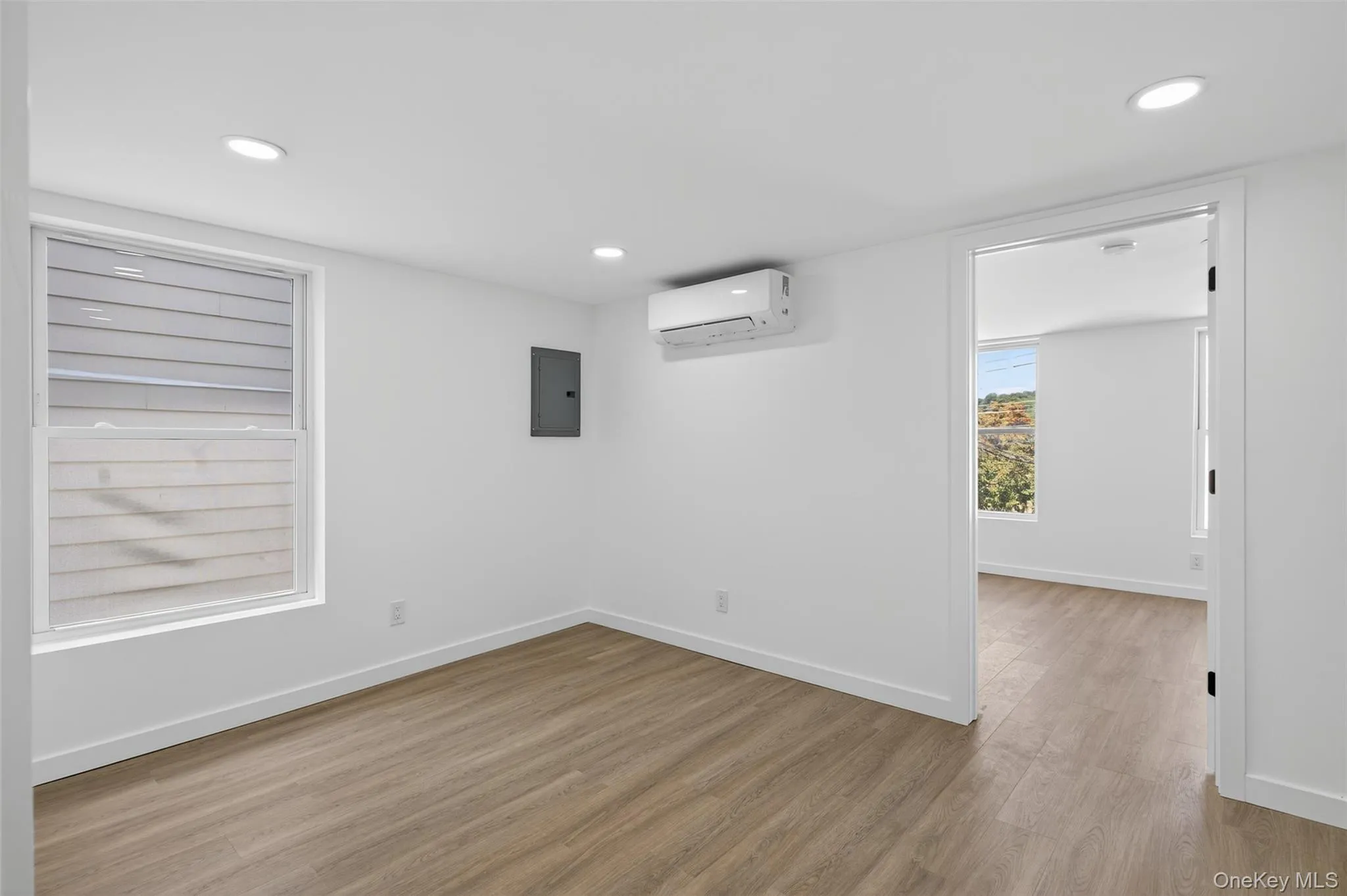 Empty room with light wood-style flooring, recessed lighting, electric panel, and a wall mounted air conditioner Empty room with light wood-style flooring, recessed lighting, electric panel, and a wall mounted air conditioner