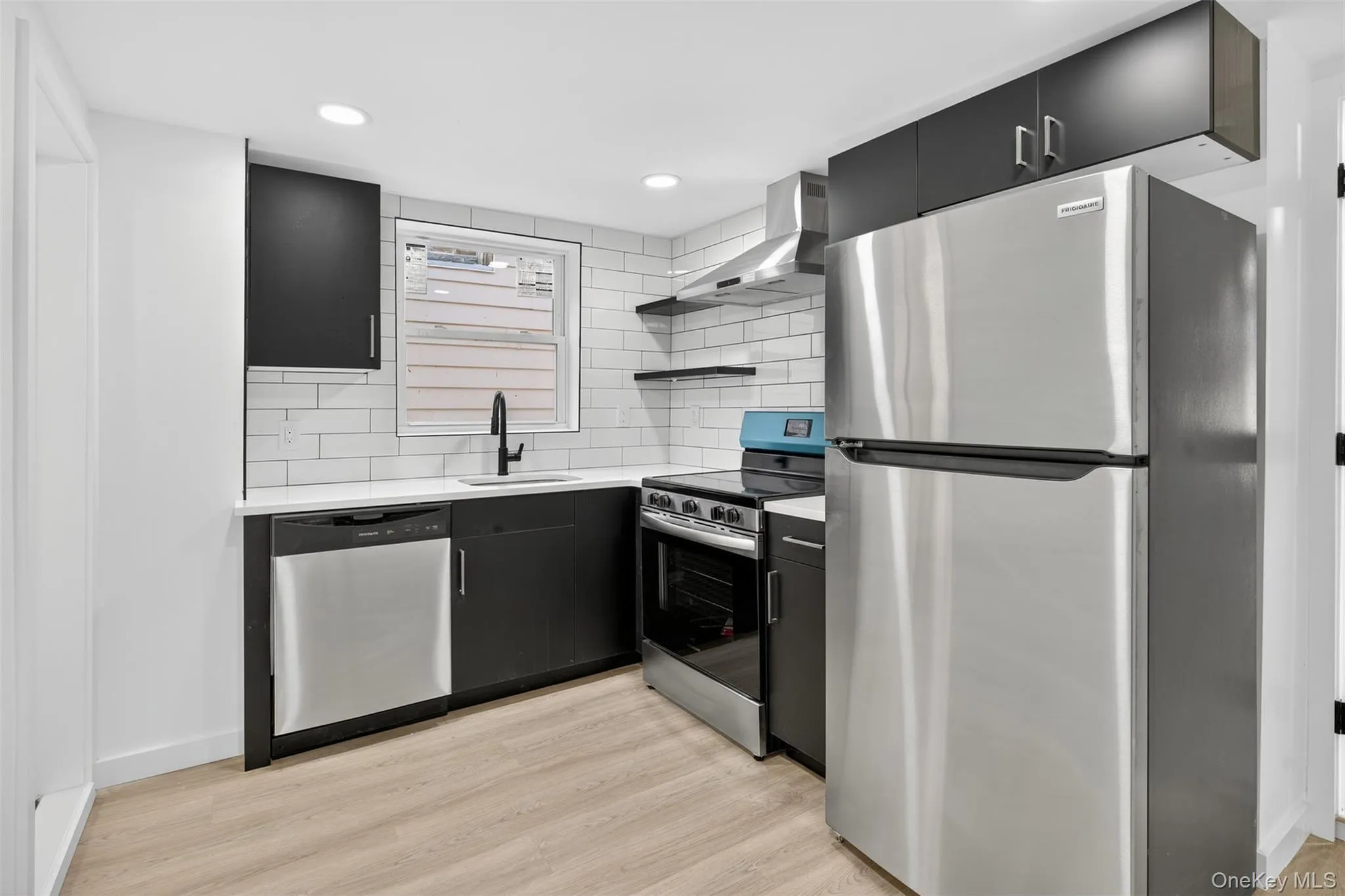 Kitchen featuring dark cabinets, stainless steel appliances, backsplash, light wood finished floors, and recessed lighting Kitchen featuring dark cabinets, stainless steel appliances, backsplash, light wood finished floors, and recessed lighting