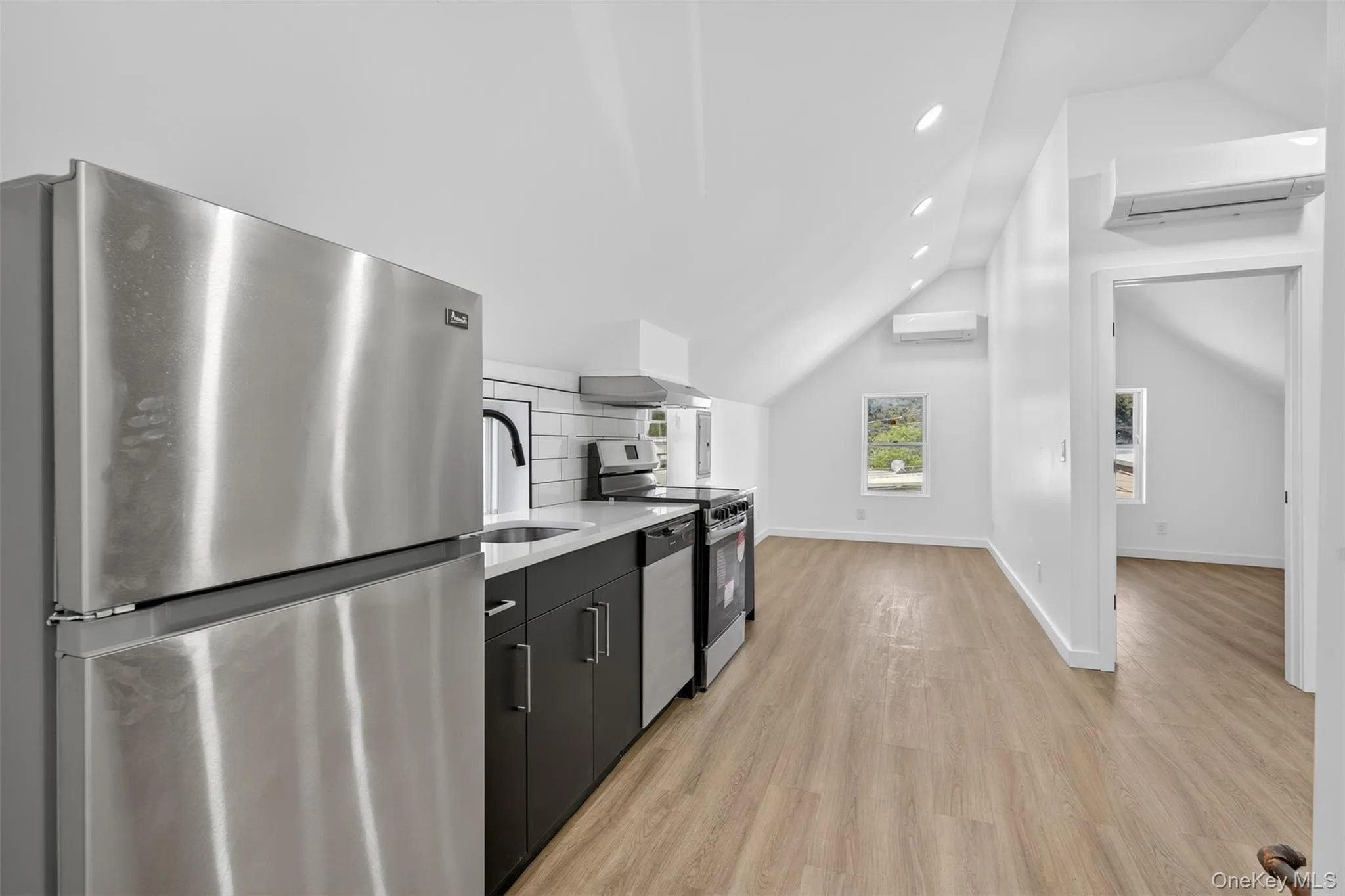 Kitchen featuring stainless steel appliances, vaulted ceiling, light wood-type flooring, recessed lighting, and an AC wall unit Kitchen featuring stainless steel appliances, vaulted ceiling, light wood-type flooring, recessed lighting, and an AC wall unit