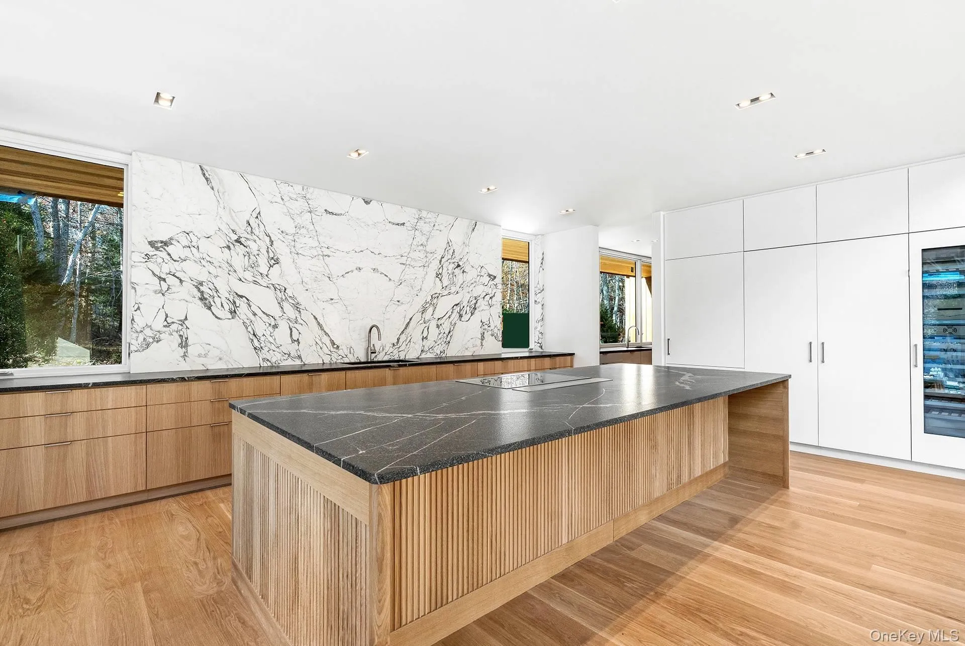Kitchen with modern cabinets, a large island, beverage cooler, white cabinets, and dark stone counters Kitchen with modern cabinets, a large island, beverage cooler, white cabinets, and dark stone counters