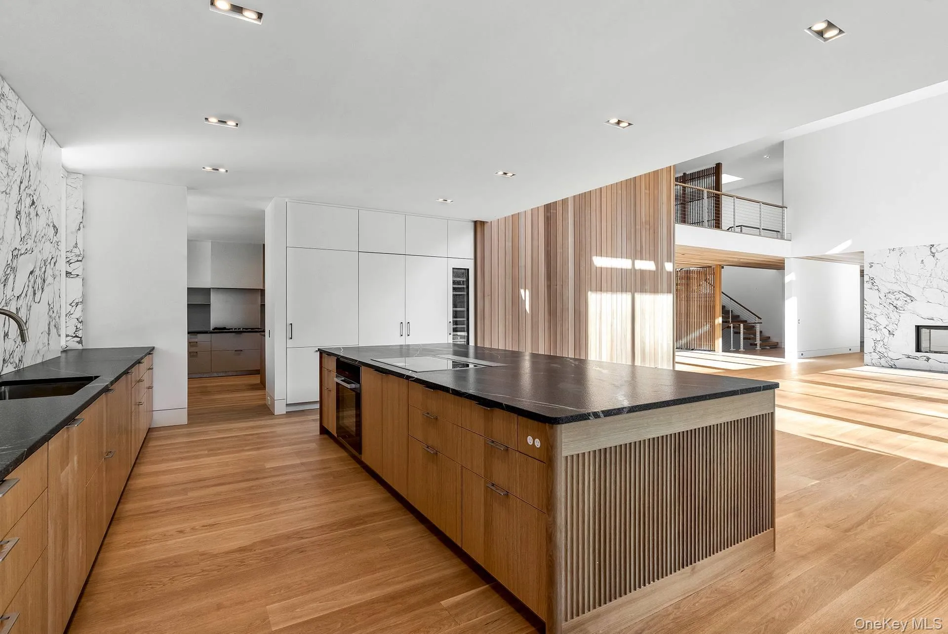 Kitchen featuring modern cabinets, a spacious island, light wood-style flooring, brown cabinetry, and dark stone counters Kitchen featuring modern cabinets, a spacious island, light wood-style flooring, brown cabinetry, and dark stone counters