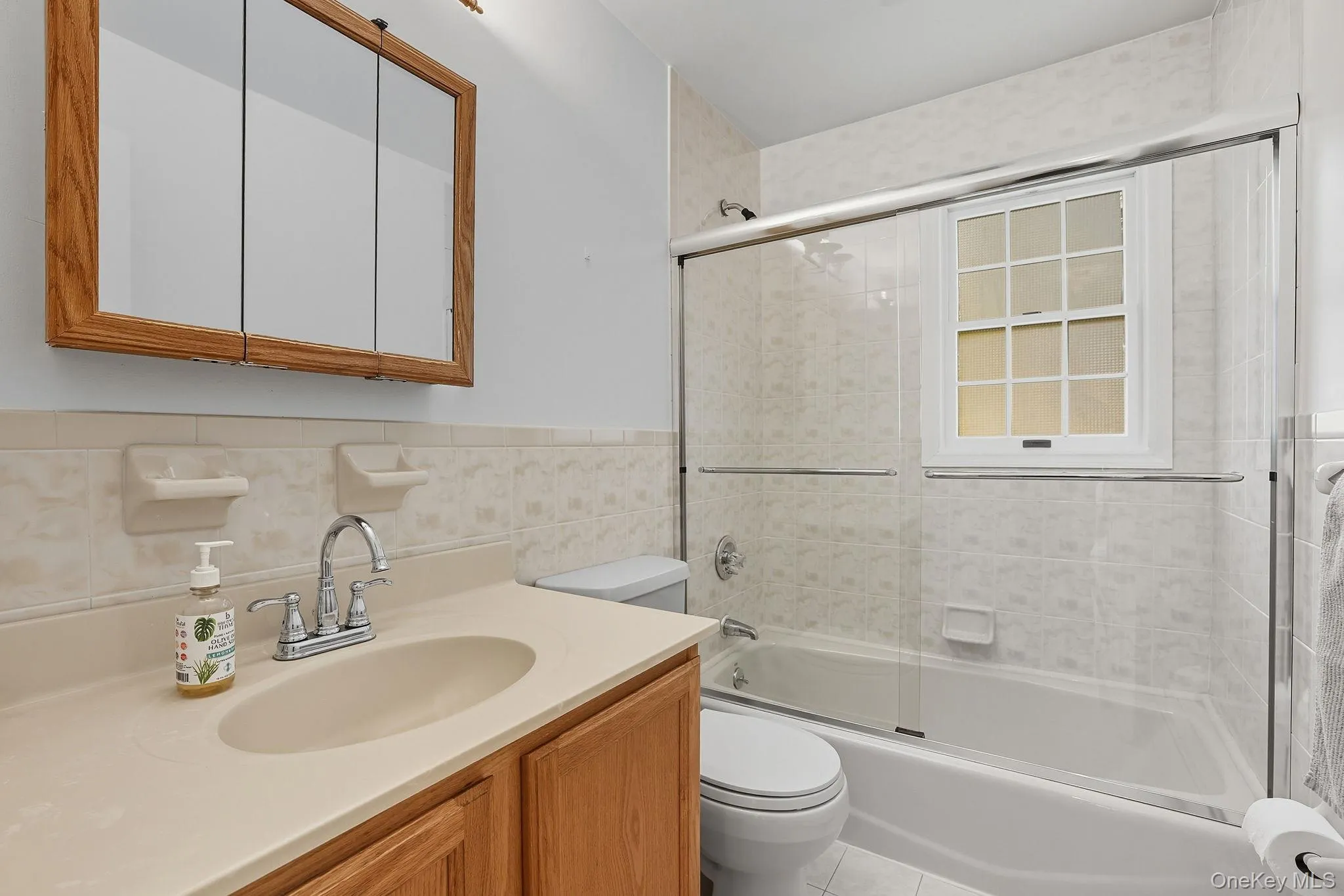Full bathroom with combined bath / shower with glass door, vanity, and tile walls Full bathroom with combined bath / shower with glass door, vanity, and tile walls