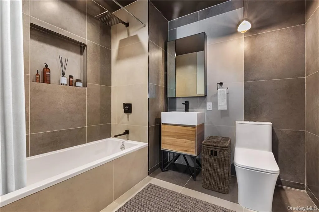 Bathroom with toilet, vanity, tile patterned flooring, tile walls, and tiled shower / bath Bathroom with toilet, vanity, tile patterned flooring, tile walls, and tiled shower / bath