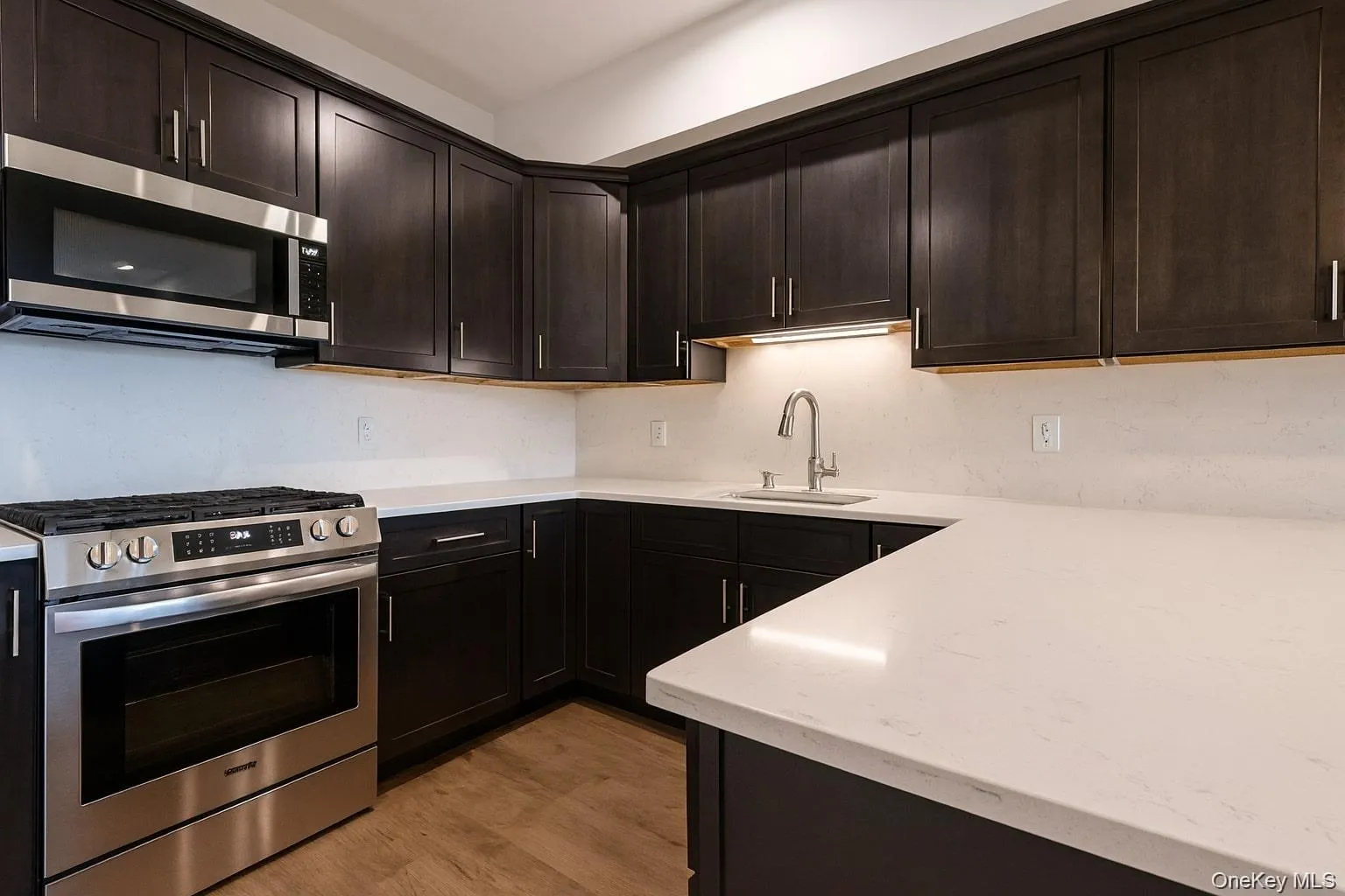 Kitchen featuring appliances with stainless steel finishes, dark brown cabinetry, light wood-style floors, and light stone countertops Kitchen featuring appliances with stainless steel finishes, dark brown cabinetry, light wood-style floors, and light stone countertops