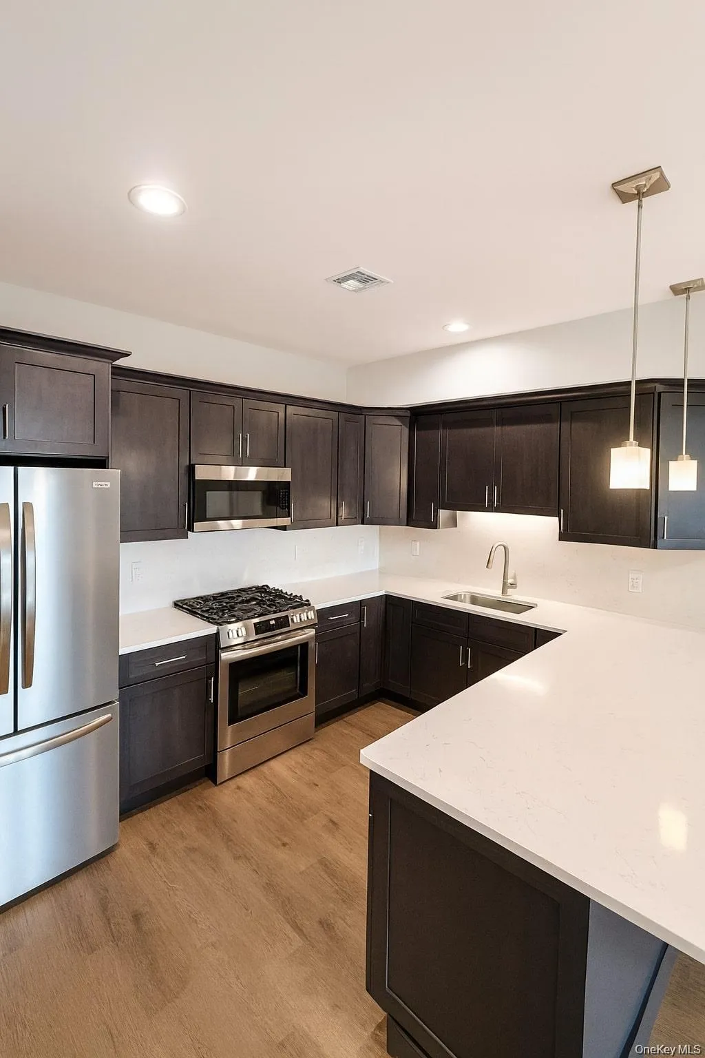 Kitchen with appliances with stainless steel finishes, hanging light fixtures, dark brown cabinets, light wood finished floors, and recessed lighting Kitchen with appliances with stainless steel finishes, hanging light fixtures, dark brown cabinets, light wood finished floors, and recessed lighting
