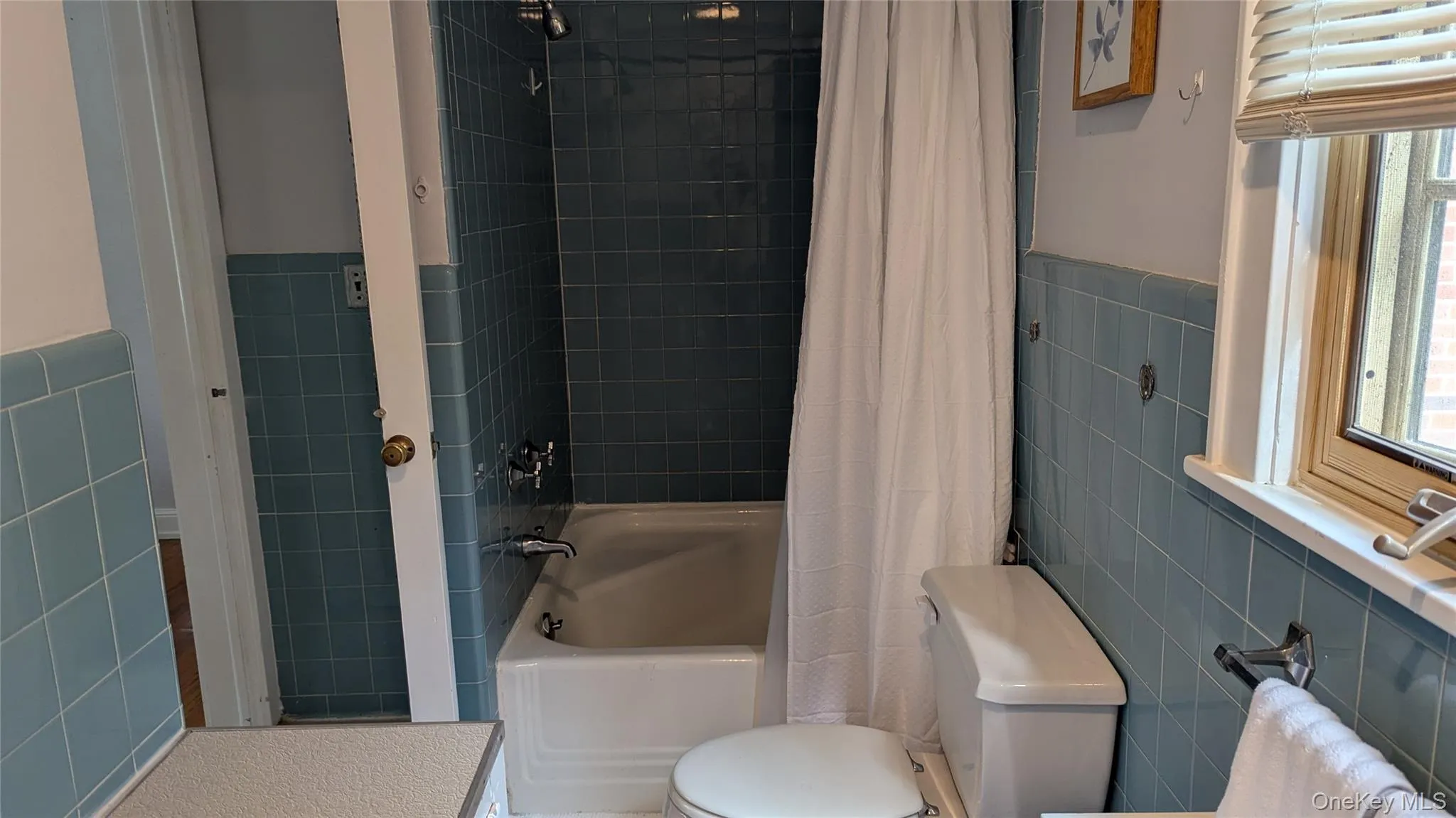 Bathroom featuring tile walls, shower / bath combination with curtain, and a wainscoted wall Bathroom featuring tile walls, shower / bath combination with curtain, and a wainscoted wall