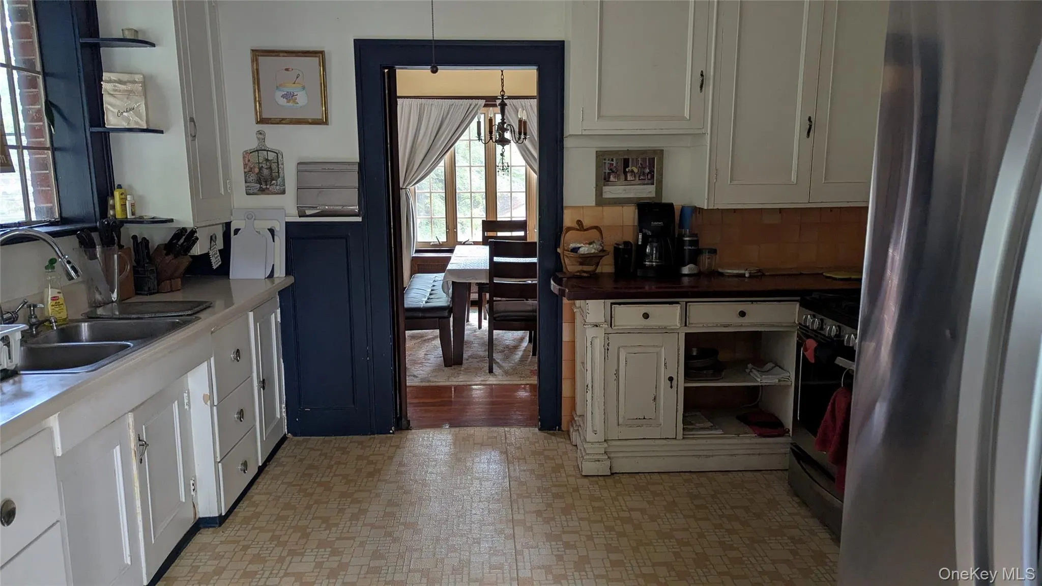 Kitchen with appliances with stainless steel finishes, white cabinetry, a chandelier, backsplash, and light floors Kitchen with appliances with stainless steel finishes, white cabinetry, a chandelier, backsplash, and light floors