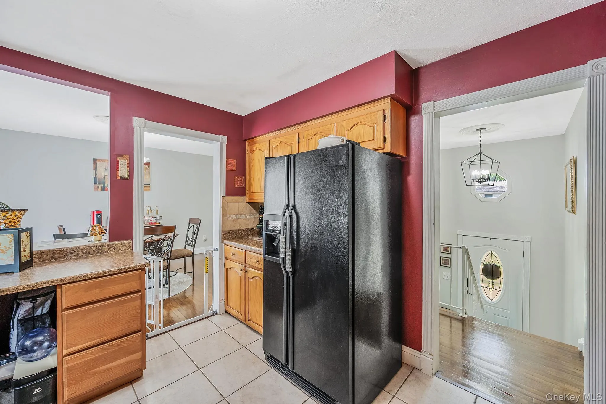 Kitchen with black fridge, backsplash, light tile patterned floors, hanging light fixtures, and light stone countertops Kitchen with black fridge, backsplash, light tile patterned floors, hanging light fixtures, and light stone countertops