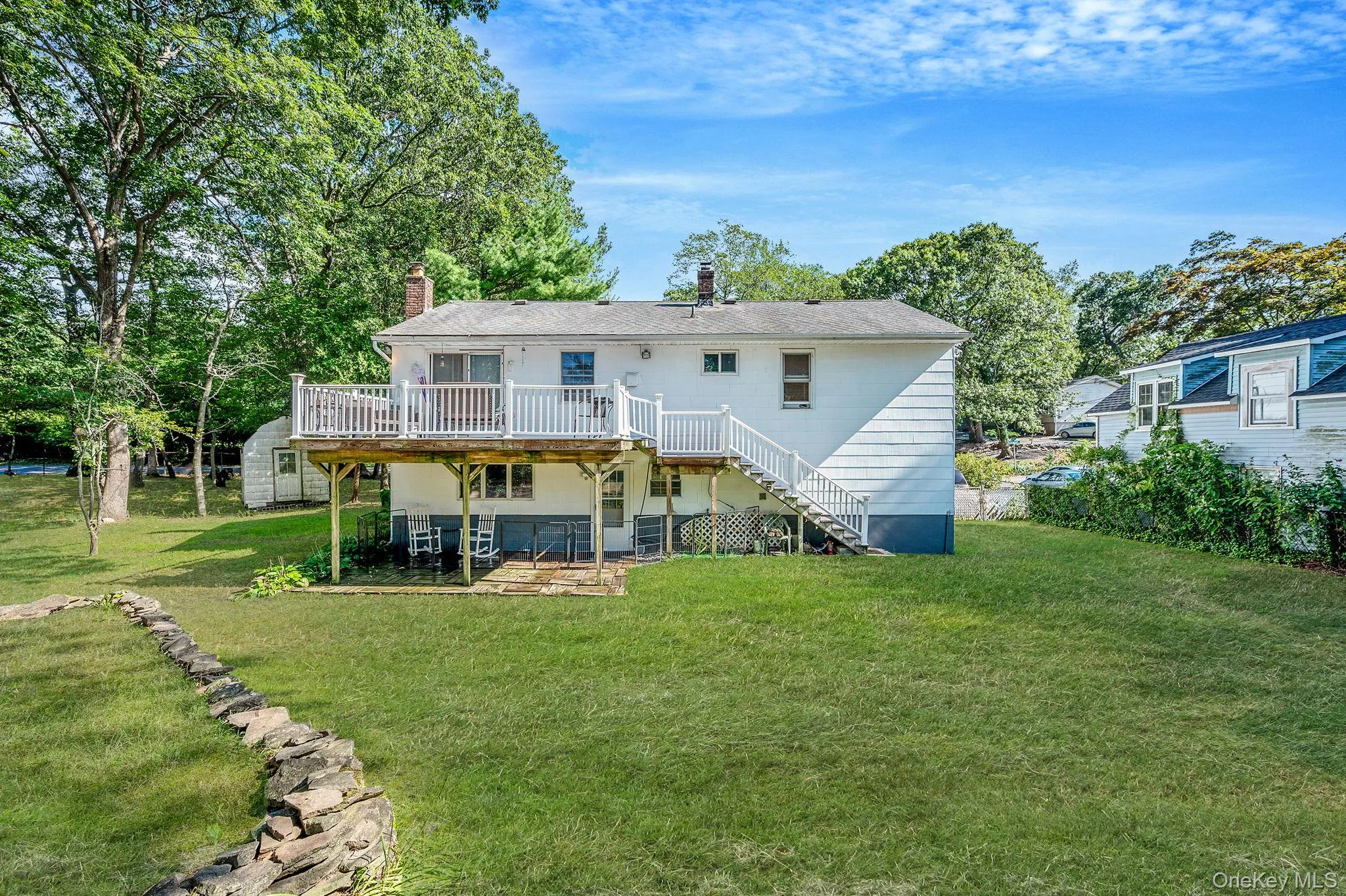 Rear view of property with a chimney, stairs, a deck, and a lawn Rear view of property with a chimney, stairs, a deck, and a lawn