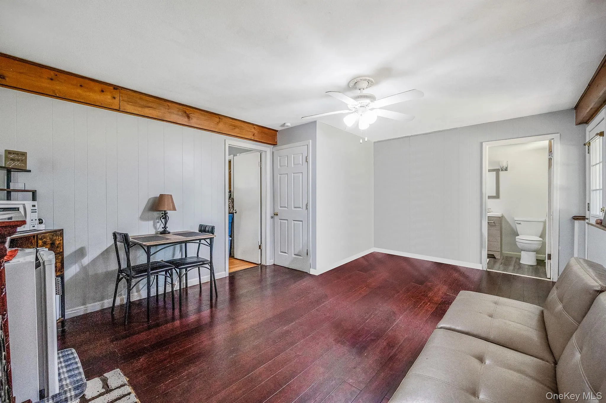 Living area featuring wood finished floors, a ceiling fan, wooden walls, and beamed ceiling Living area featuring wood finished floors, a ceiling fan, wooden walls, and beamed ceiling