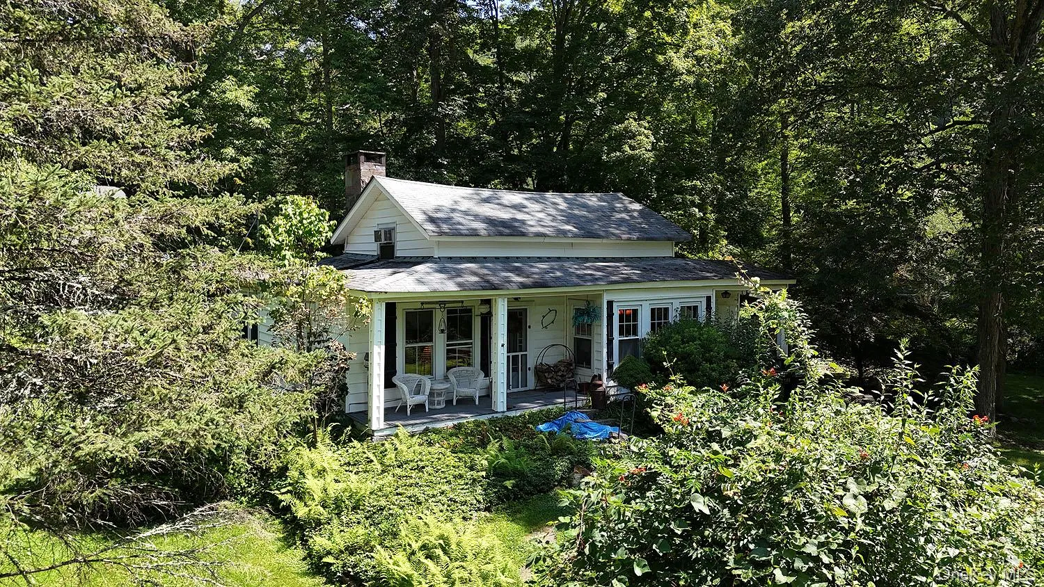 View of front facade with a porch, a chimney, a shingled roof, and a wooded view View of front facade with a porch, a chimney, a shingled roof, and a wooded view