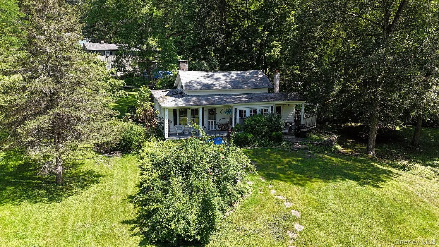 View of front of home featuring a porch, a chimney, a front lawn, and a forest view View of front of home featuring a porch, a chimney, a front lawn, and a forest view