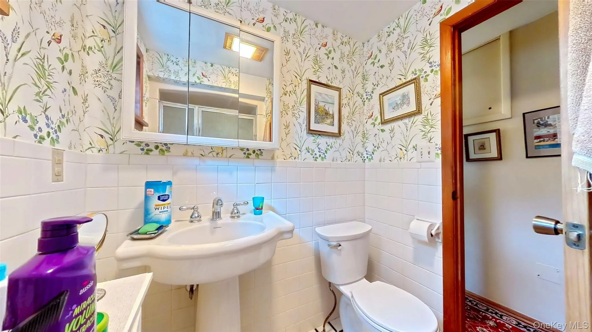 Updated bathroom with a shower stall, tile walls, wainscoting, and wallpapered walls Updated bathroom with a shower stall, tile walls, wainscoting, and wallpapered walls