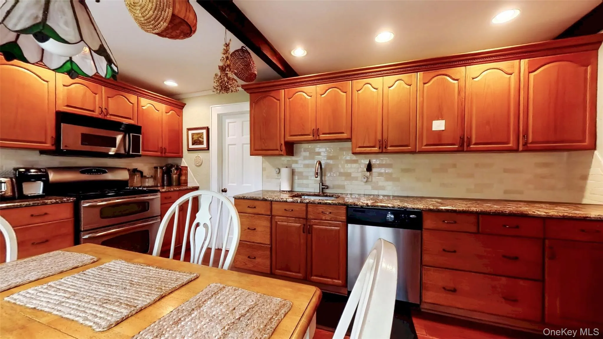 Kitchen featuring dark granite counters, stainless steel appliances, custom backsplash, beam ceiling, and recessed lighting Kitchen featuring dark granite counters, stainless steel appliances, custom backsplash, beam ceiling, and recessed lighting