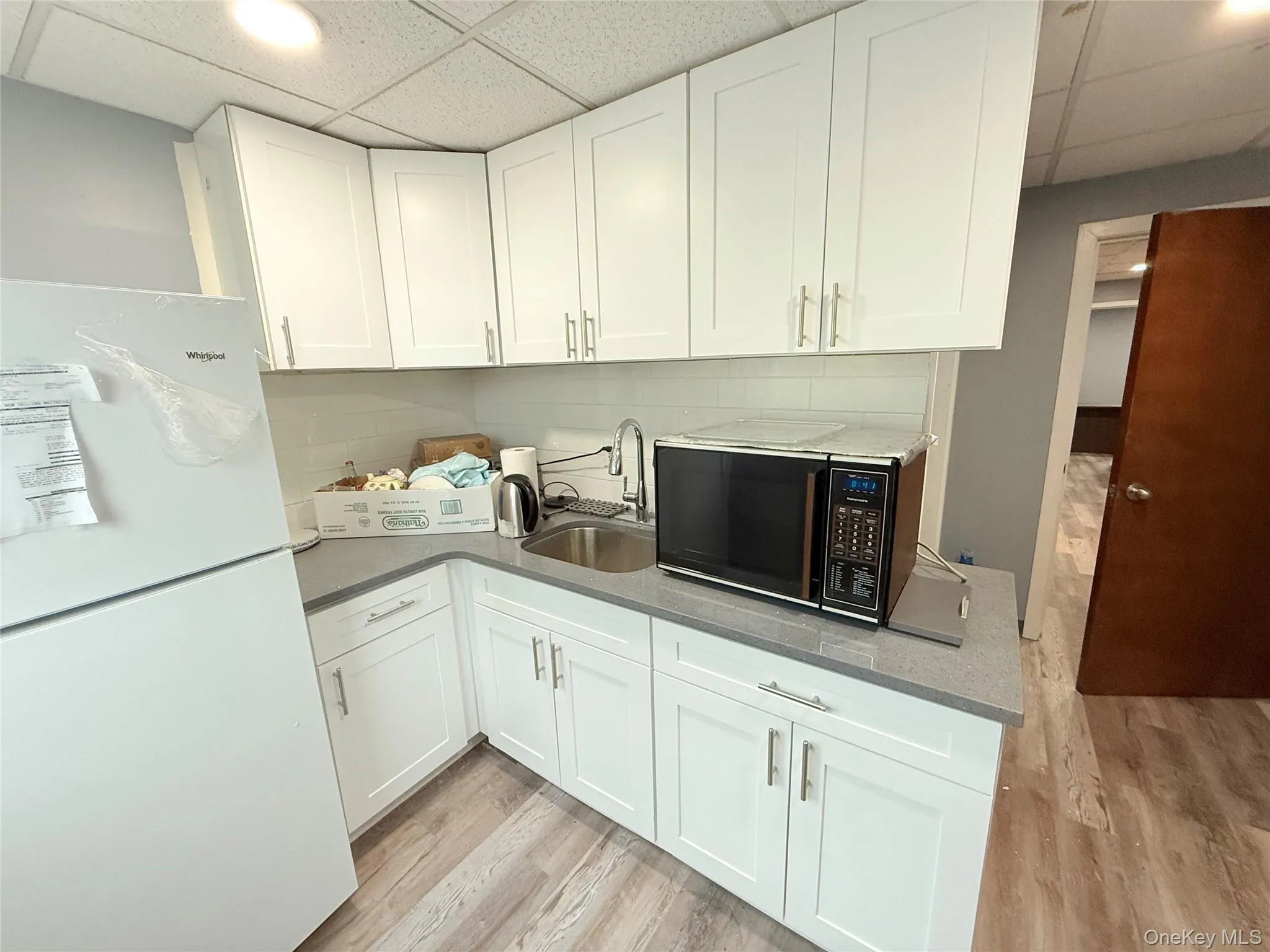 Kitchen featuring a drop ceiling, freestanding refrigerator, white cabinets, light wood finished floors, and decorative backsplash Kitchen featuring a drop ceiling, freestanding refrigerator, white cabinets, light wood finished floors, and decorative backsplash