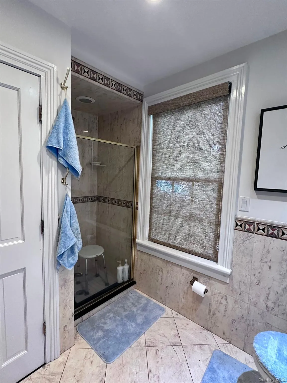 Bathroom with a stall shower, light tile patterned flooring, tile walls, and a wainscoted wall Bathroom with a stall shower, light tile patterned flooring, tile walls, and a wainscoted wall