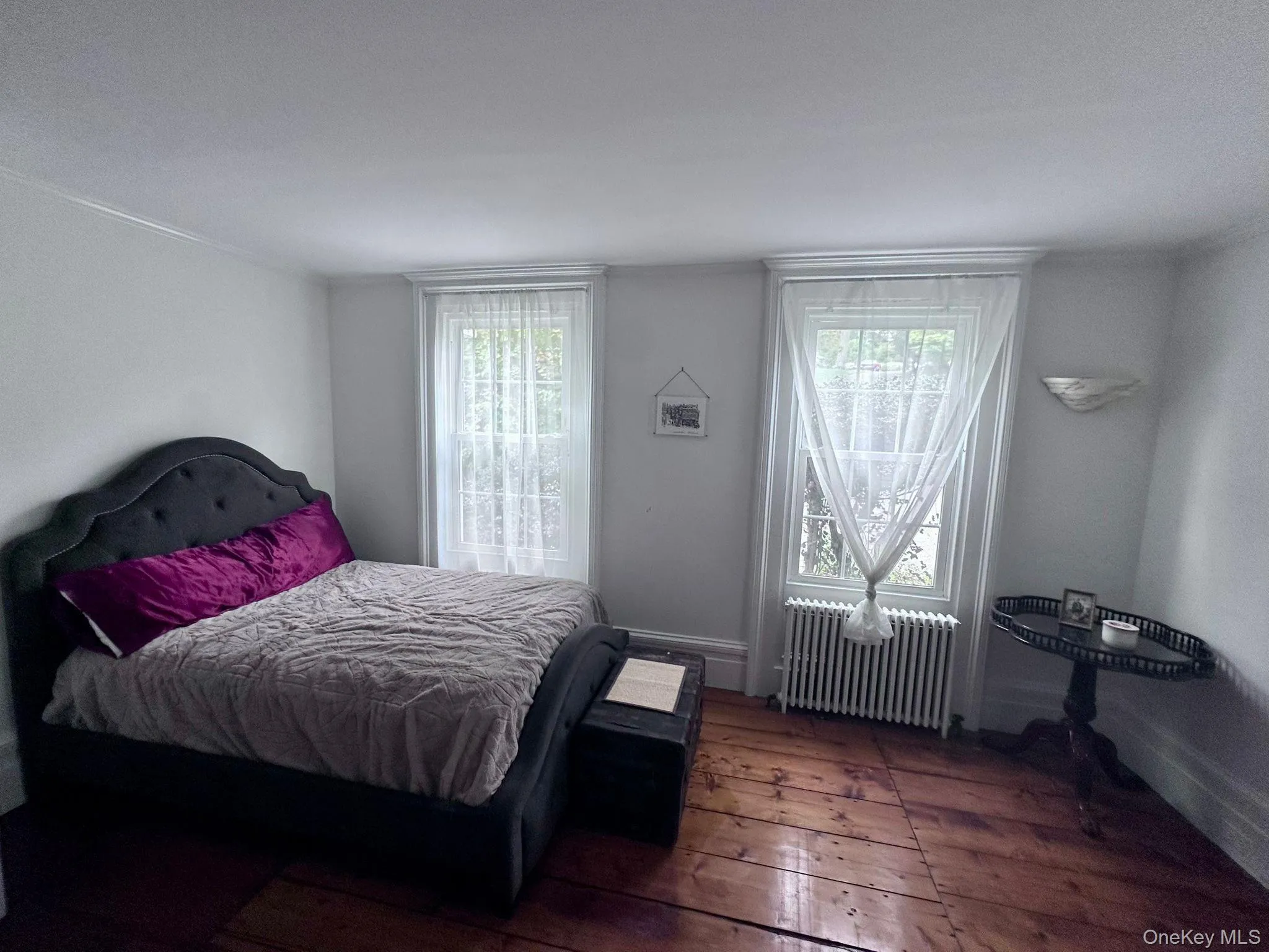 Bedroom featuring multiple windows, radiator, and wood-type flooring Bedroom featuring multiple windows, radiator, and wood-type flooring