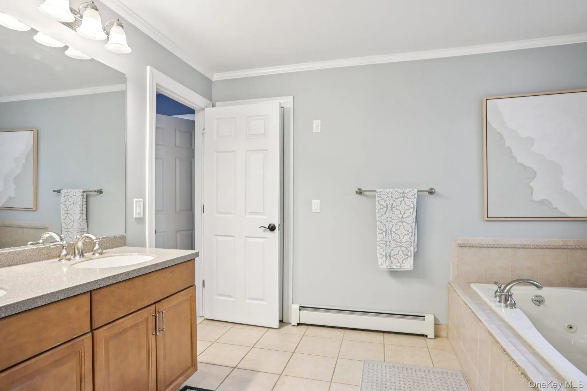 Bathroom featuring light tile patterned floors, crown molding, double vanity, a baseboard radiator, and a tub with jets Bathroom featuring light tile patterned floors, crown molding, double vanity, a baseboard radiator, and a tub with jets