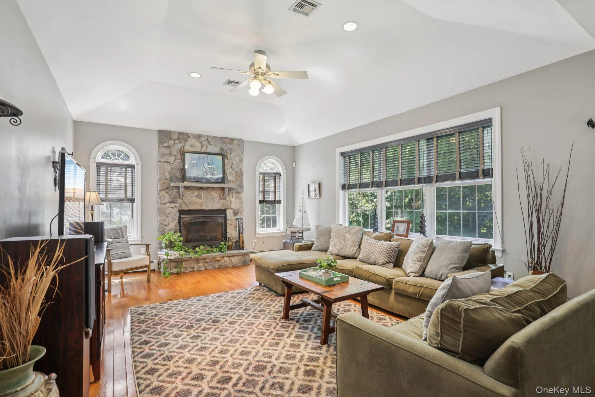 Living room with healthy amount of natural light, wood-type flooring, a stone fireplace, a ceiling fan, and recessed lighting Living room with healthy amount of natural light, wood-type flooring, a stone fireplace, a ceiling fan, and recessed lighting