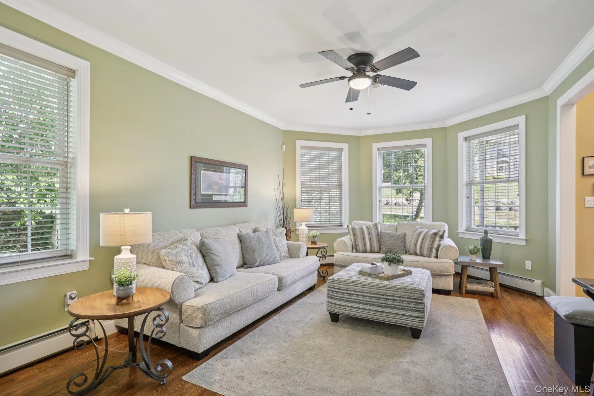 Living area featuring crown molding, baseboard heating, dark wood-style floors, and ceiling fan Living area featuring crown molding, baseboard heating, dark wood-style floors, and ceiling fan