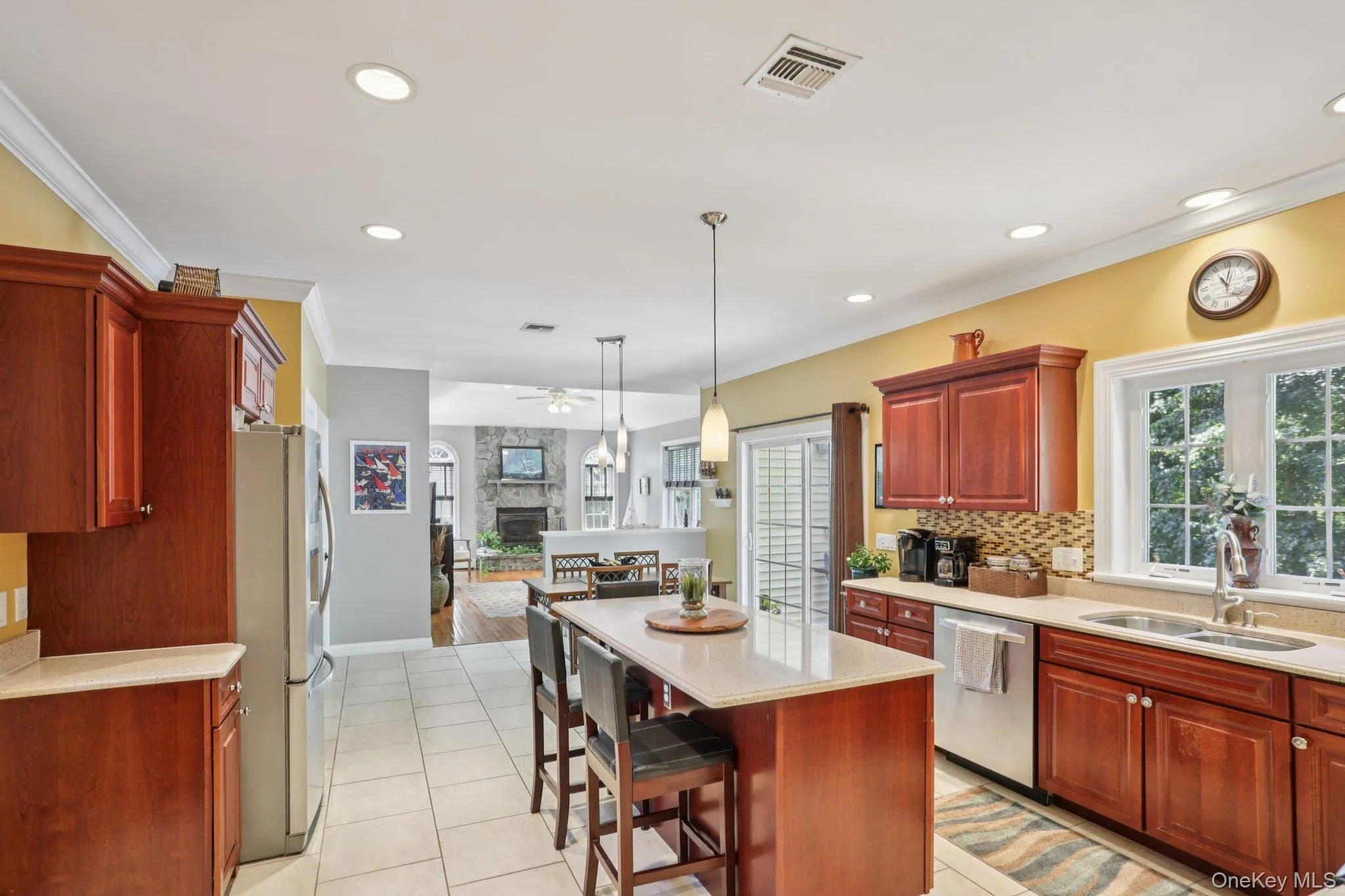 Kitchen featuring ornamental molding, decorative light fixtures, a stone fireplace, appliances with stainless steel finishes, and a center island Kitchen featuring ornamental molding, decorative light fixtures, a stone fireplace, appliances with stainless steel finishes, and a center island