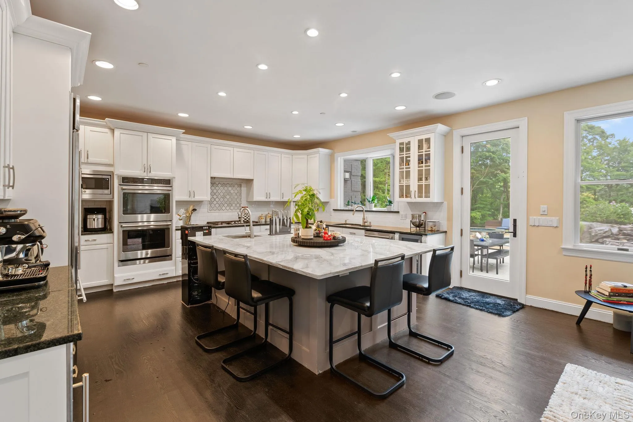 Kitchen featuring tasteful backsplash, light stone counters, a breakfast bar, an island with sink, and white cabinets Kitchen featuring tasteful backsplash, light stone counters, a breakfast bar, an island with sink, and white cabinets