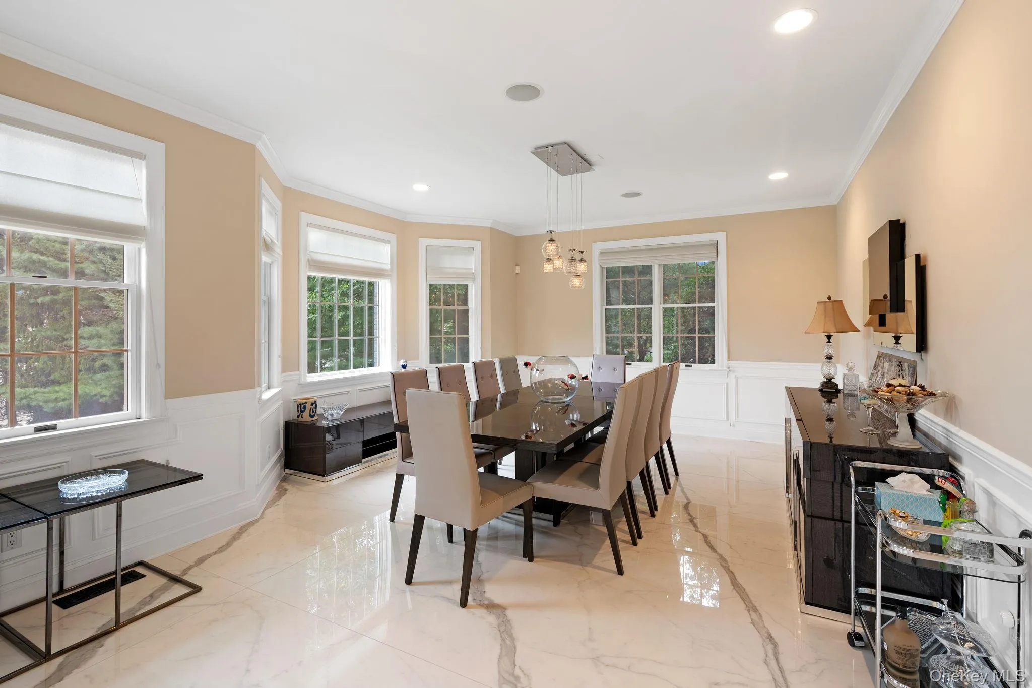 Dining space featuring light marble finish floors, a wainscoted wall, a decorative wall, crown molding, and a chandelier Dining space featuring light marble finish floors, a wainscoted wall, a decorative wall, crown molding, and a chandelier