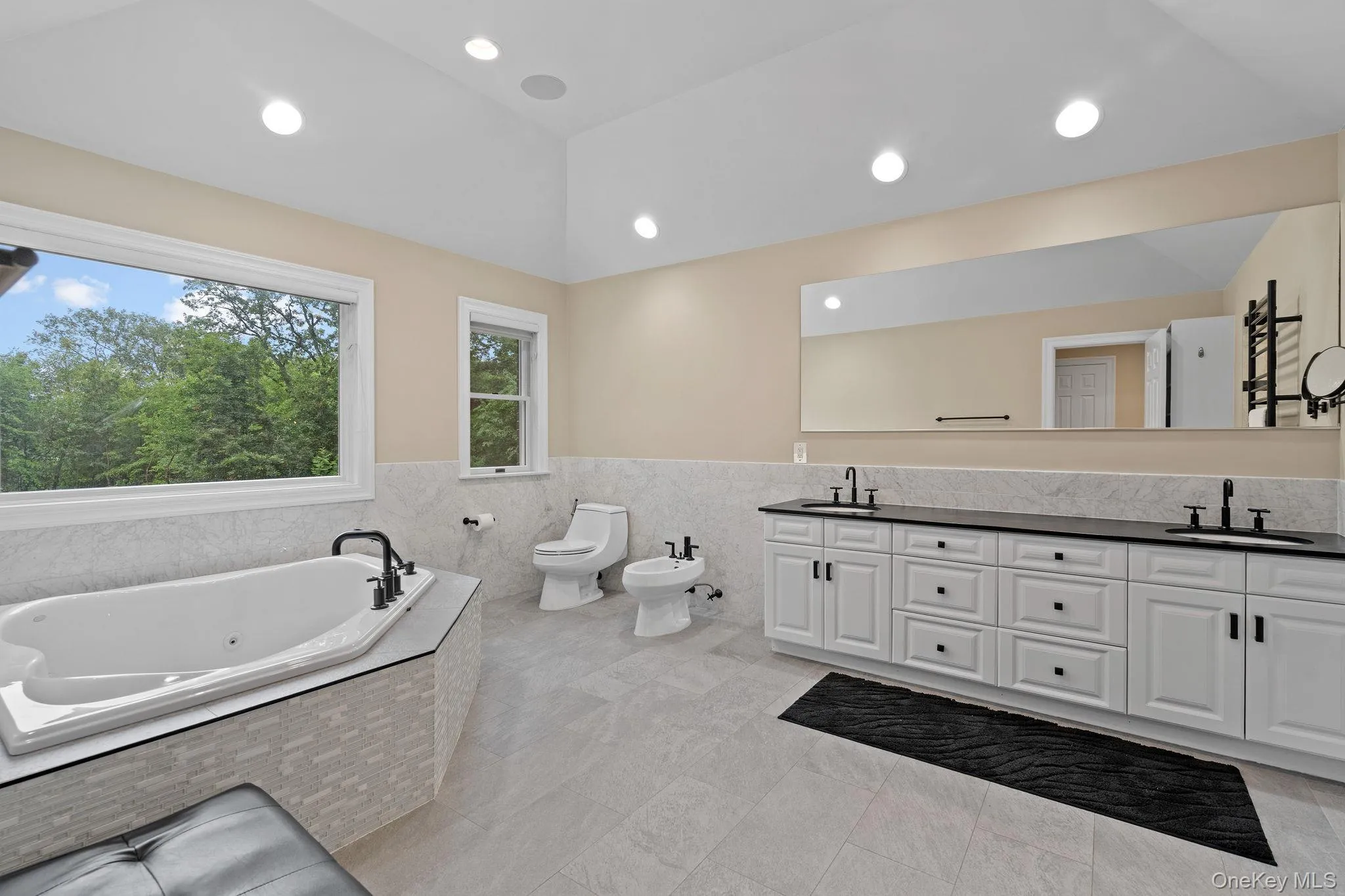 Full bathroom featuring tile walls, a jetted tub, double vanity, wainscoting, and a bidet Full bathroom featuring tile walls, a jetted tub, double vanity, wainscoting, and a bidet