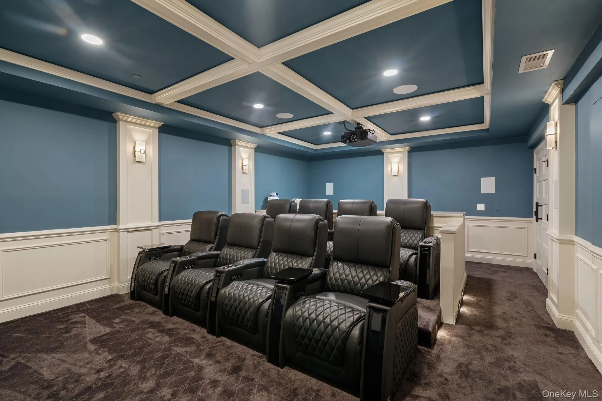 Cinema featuring a decorative wall, wainscoting, dark colored carpet, coffered ceiling, and beam ceiling Cinema featuring a decorative wall, wainscoting, dark colored carpet, coffered ceiling, and beam ceiling