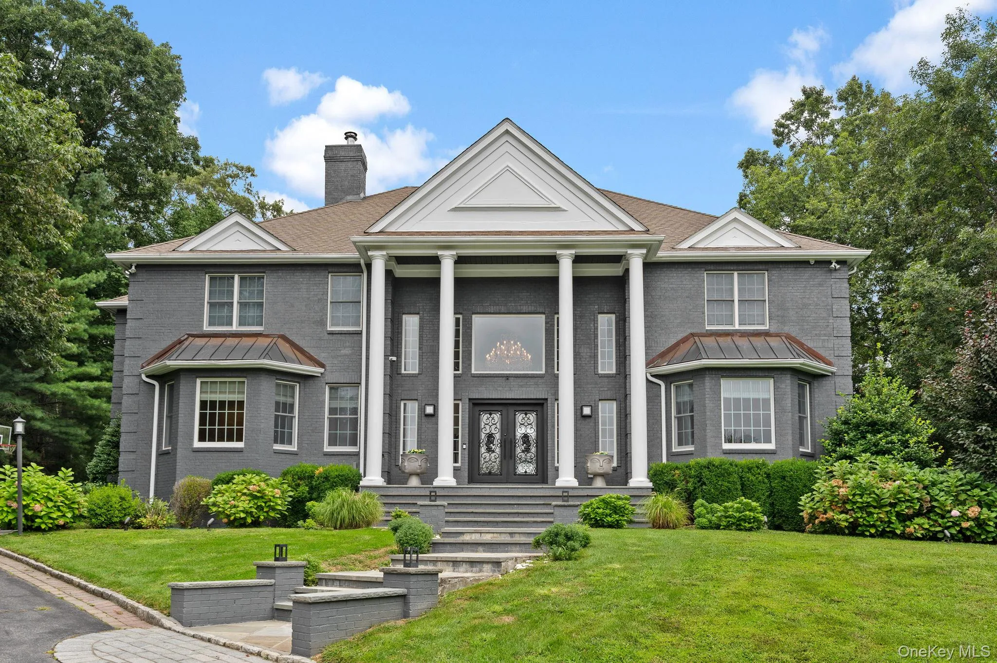Greek revival inspired property featuring a standing seam roof, brick siding, a metal roof, a chimney, and a front yard Greek revival inspired property featuring a standing seam roof, brick siding, a metal roof, a chimney, and a front yard