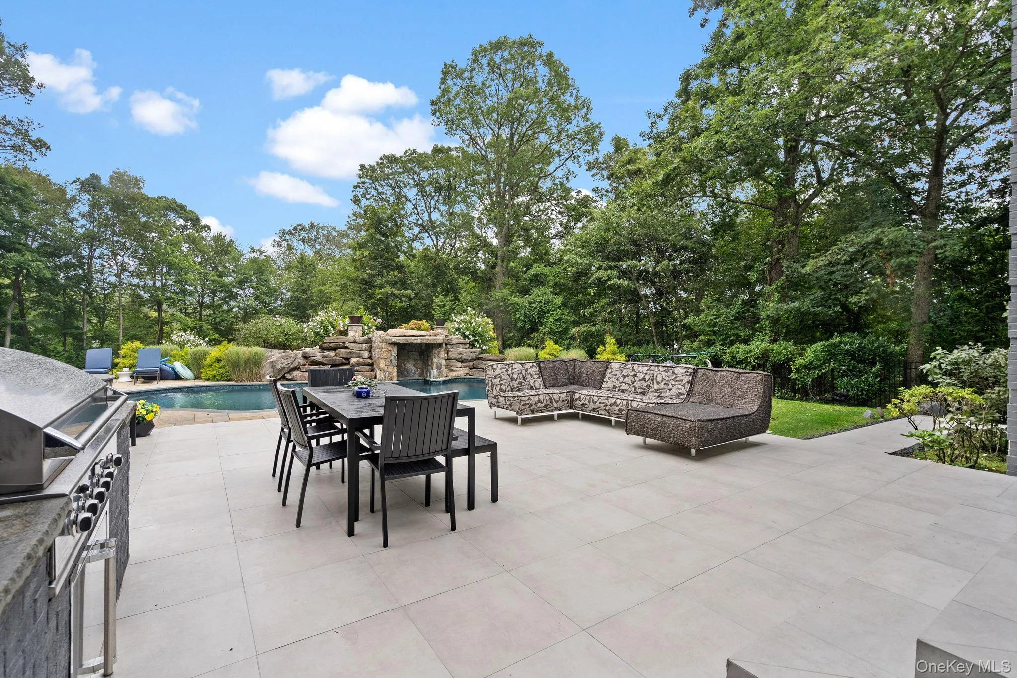 View of patio / terrace featuring an outdoor pool, outdoor dining space, view of wooded area, area for grilling, and an outdoor living space View of patio / terrace featuring an outdoor pool, outdoor dining space, view of wooded area, area for grilling, and an outdoor living space
