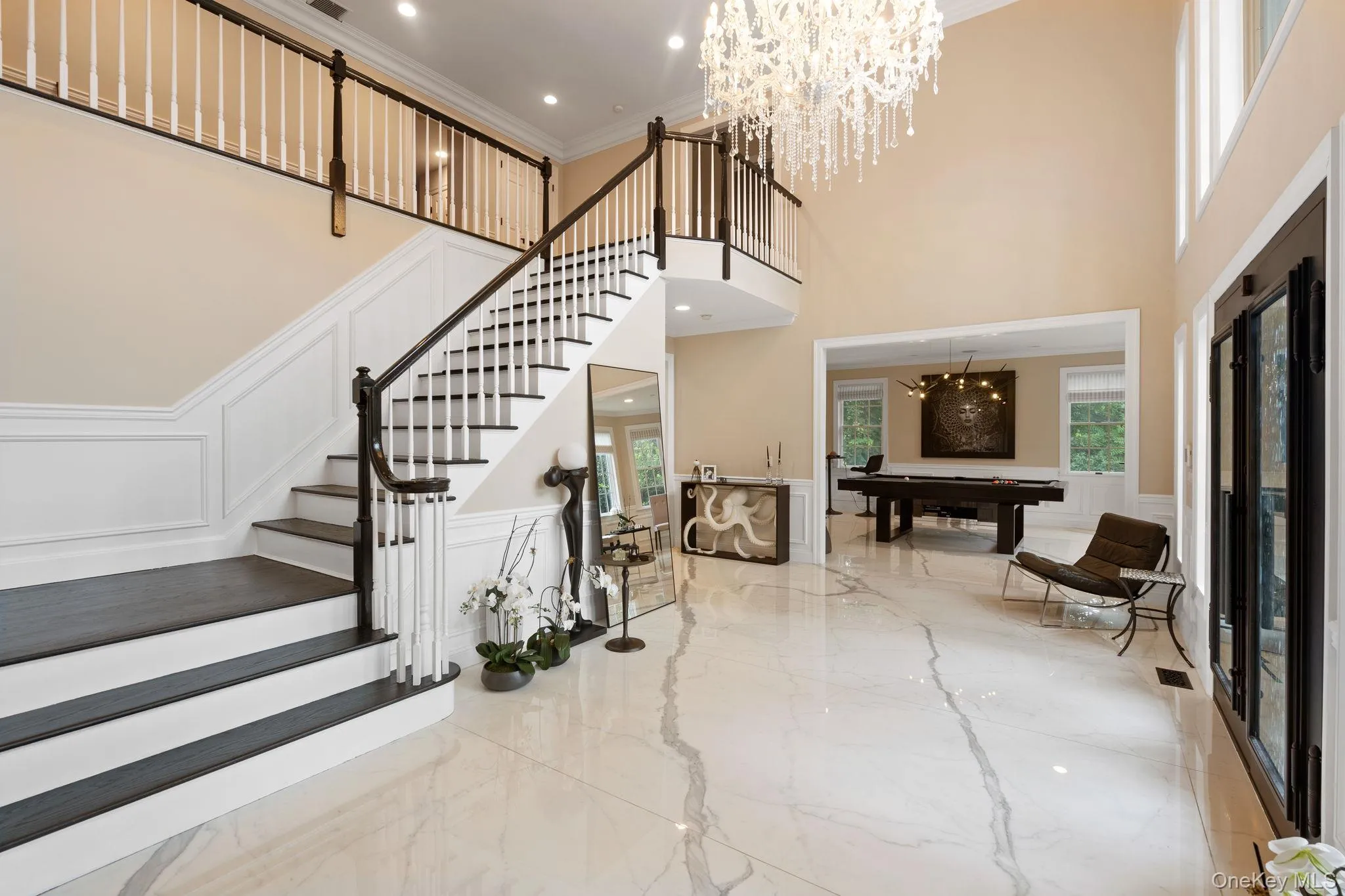 Entryway featuring a decorative wall, marble tiled floors, a chandelier, ornamental molding, and a wainscoted wall Entryway featuring a decorative wall, marble tiled floors, a chandelier, ornamental molding, and a wainscoted wall