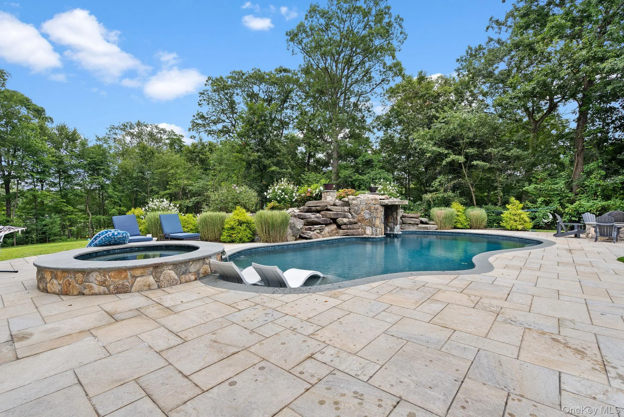 Outdoor pool featuring a patio area, an in-ground hot tub, and view of wooded area Outdoor pool featuring a patio area, an in-ground hot tub, and view of wooded area