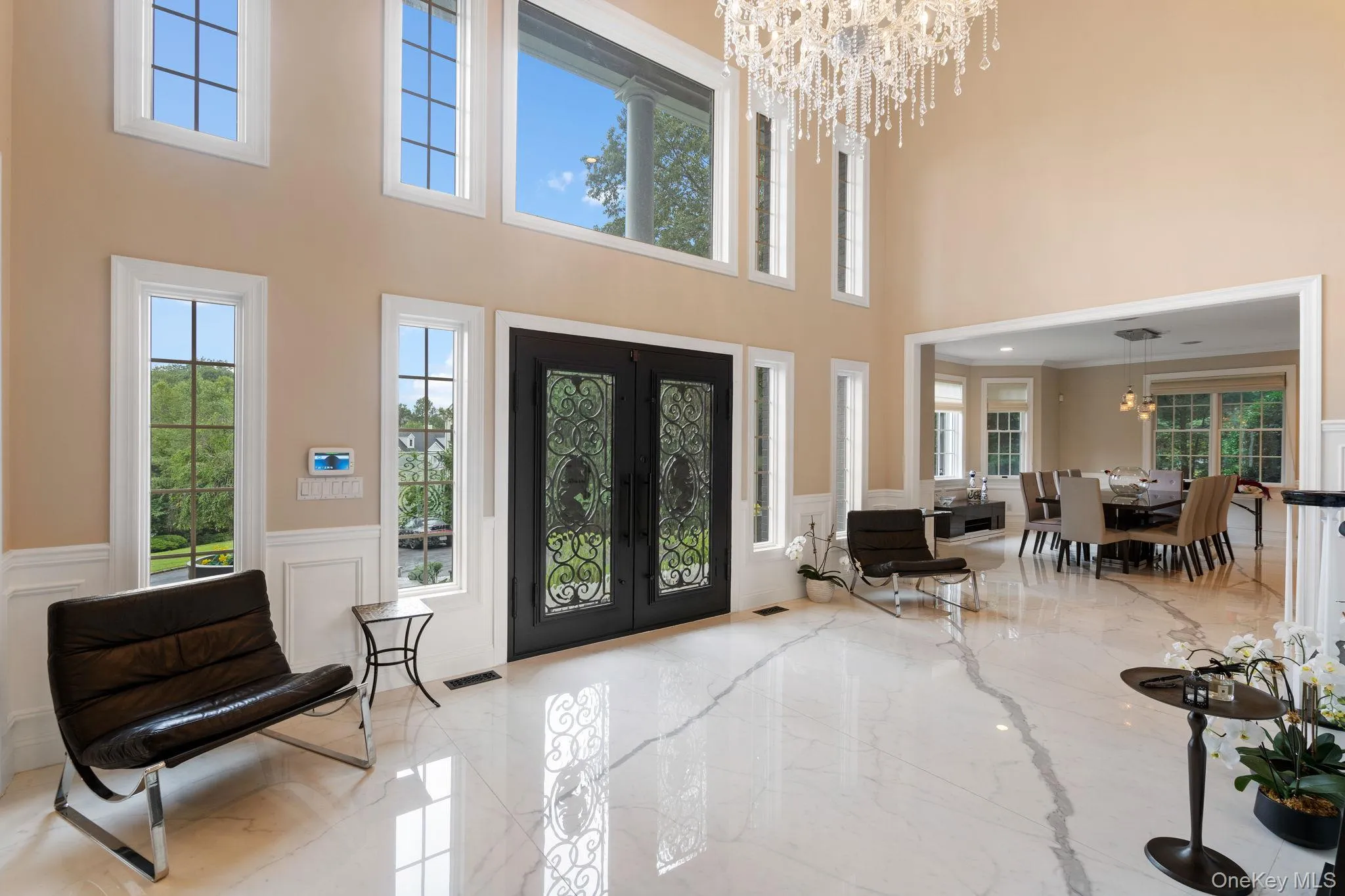 Foyer featuring a chandelier, french doors, light marble finish floors, a decorative wall, and a towering ceiling Foyer featuring a chandelier, french doors, light marble finish floors, a decorative wall, and a towering ceiling