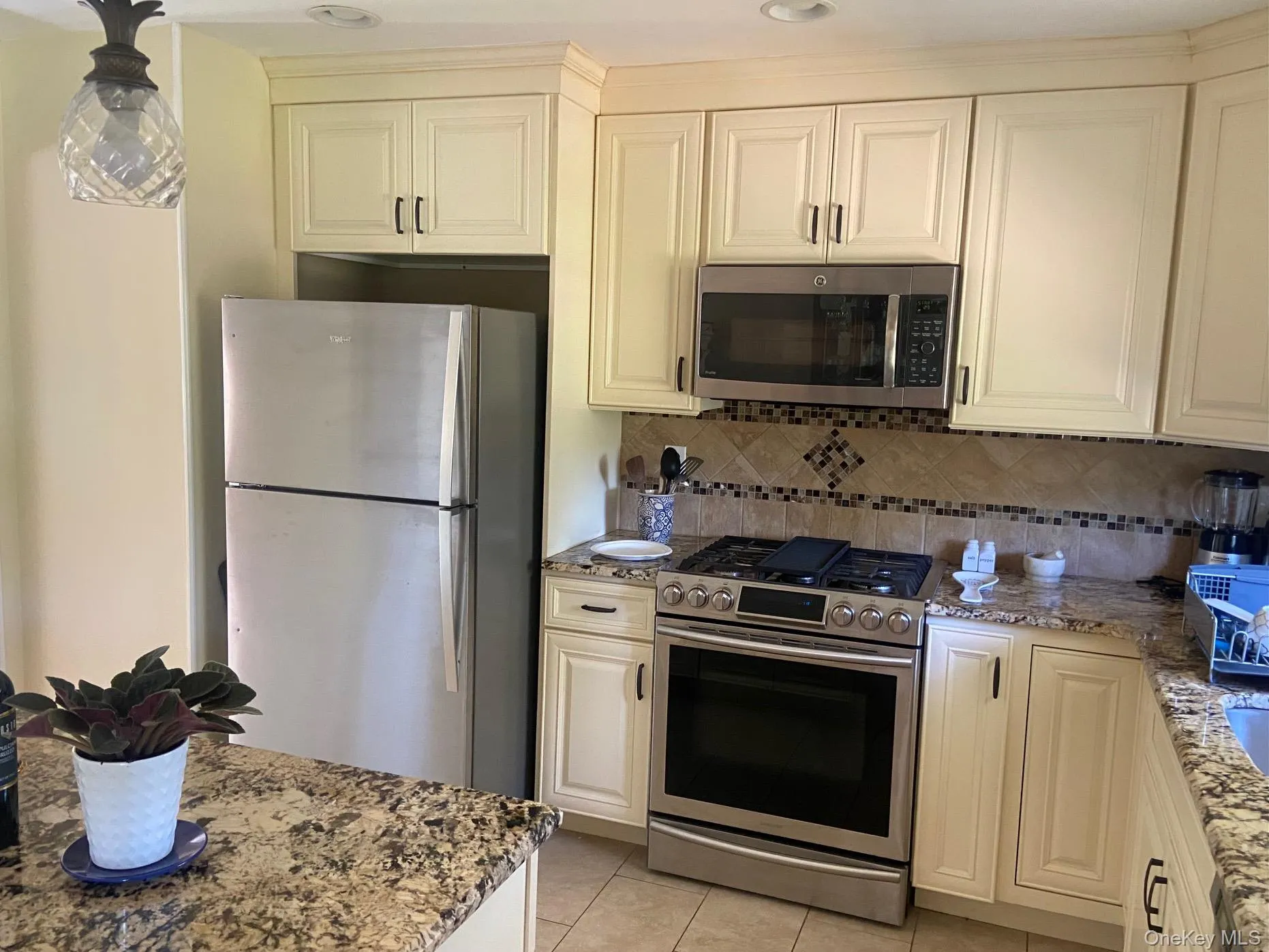 Kitchen featuring appliances with stainless steel finishes, light stone counters, light tile patterned flooring, and tasteful backsplash Kitchen featuring appliances with stainless steel finishes, light stone counters, light tile patterned flooring, and tasteful backsplash
