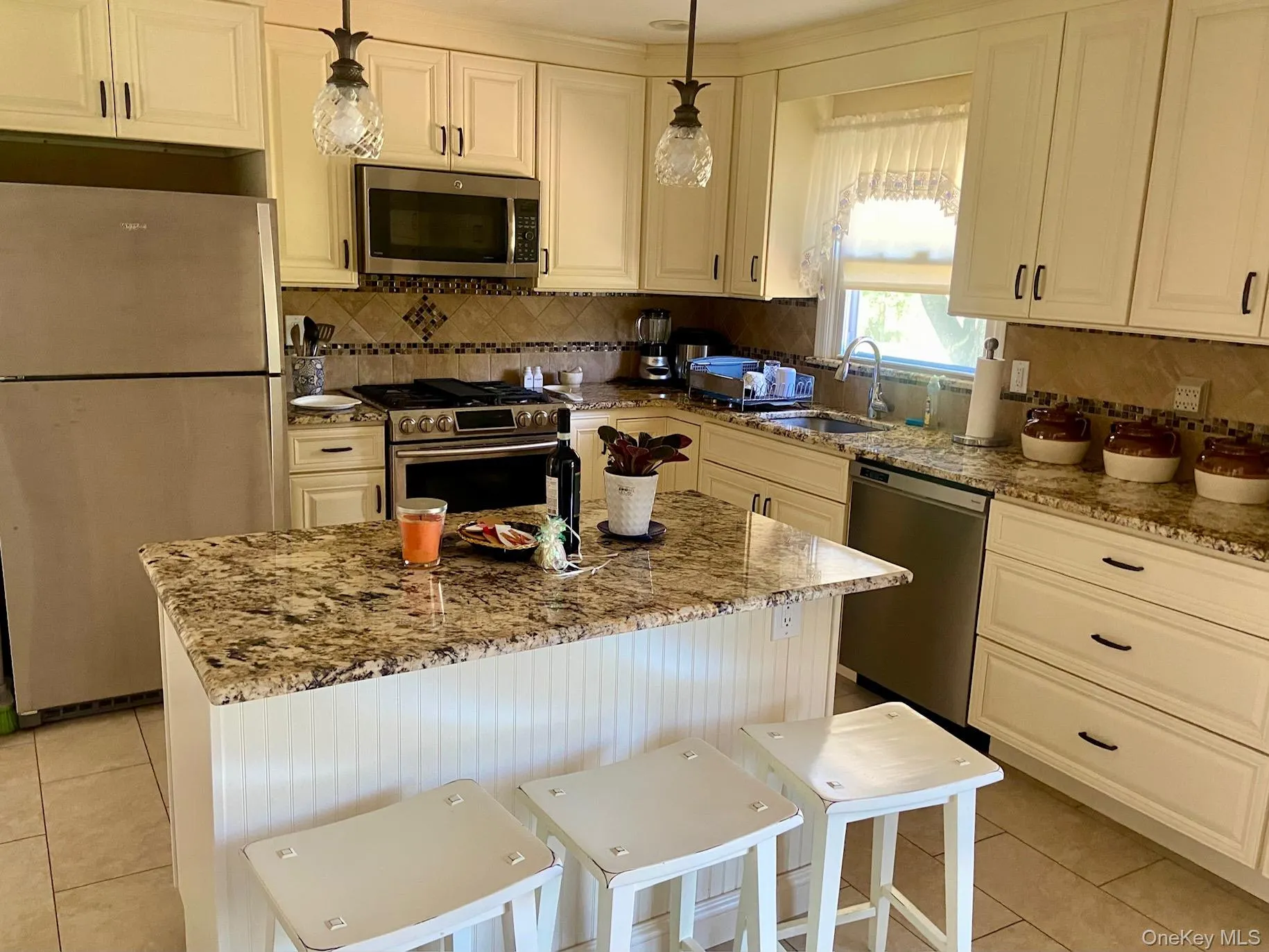 Kitchen featuring stainless steel appliances, light tile patterned floors, light stone countertops, and a kitchen island Kitchen featuring stainless steel appliances, light tile patterned floors, light stone countertops, and a kitchen island