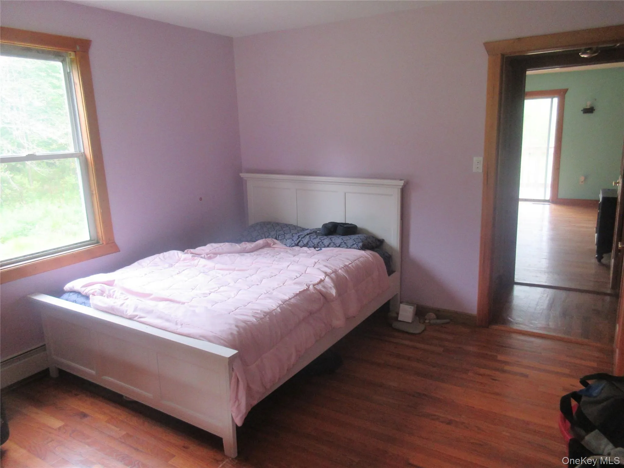 Bedroom featuring multiple windows, wood finished floors, and a baseboard heating unit Bedroom featuring multiple windows, wood finished floors, and a baseboard heating unit