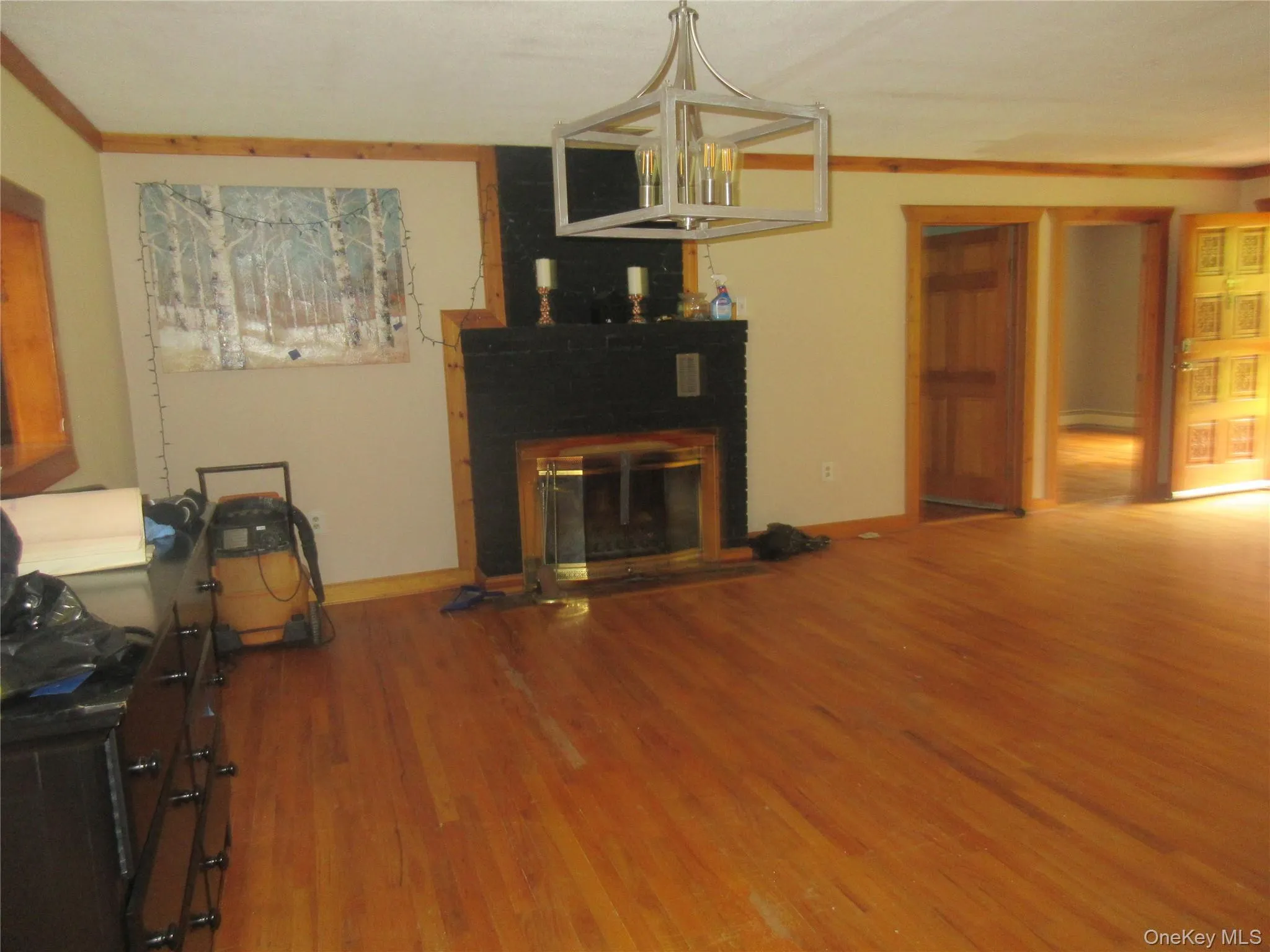 Unfurnished living room featuring wood finished floors, a fireplace, a chandelier, and ornamental molding Unfurnished living room featuring wood finished floors, a fireplace, a chandelier, and ornamental molding