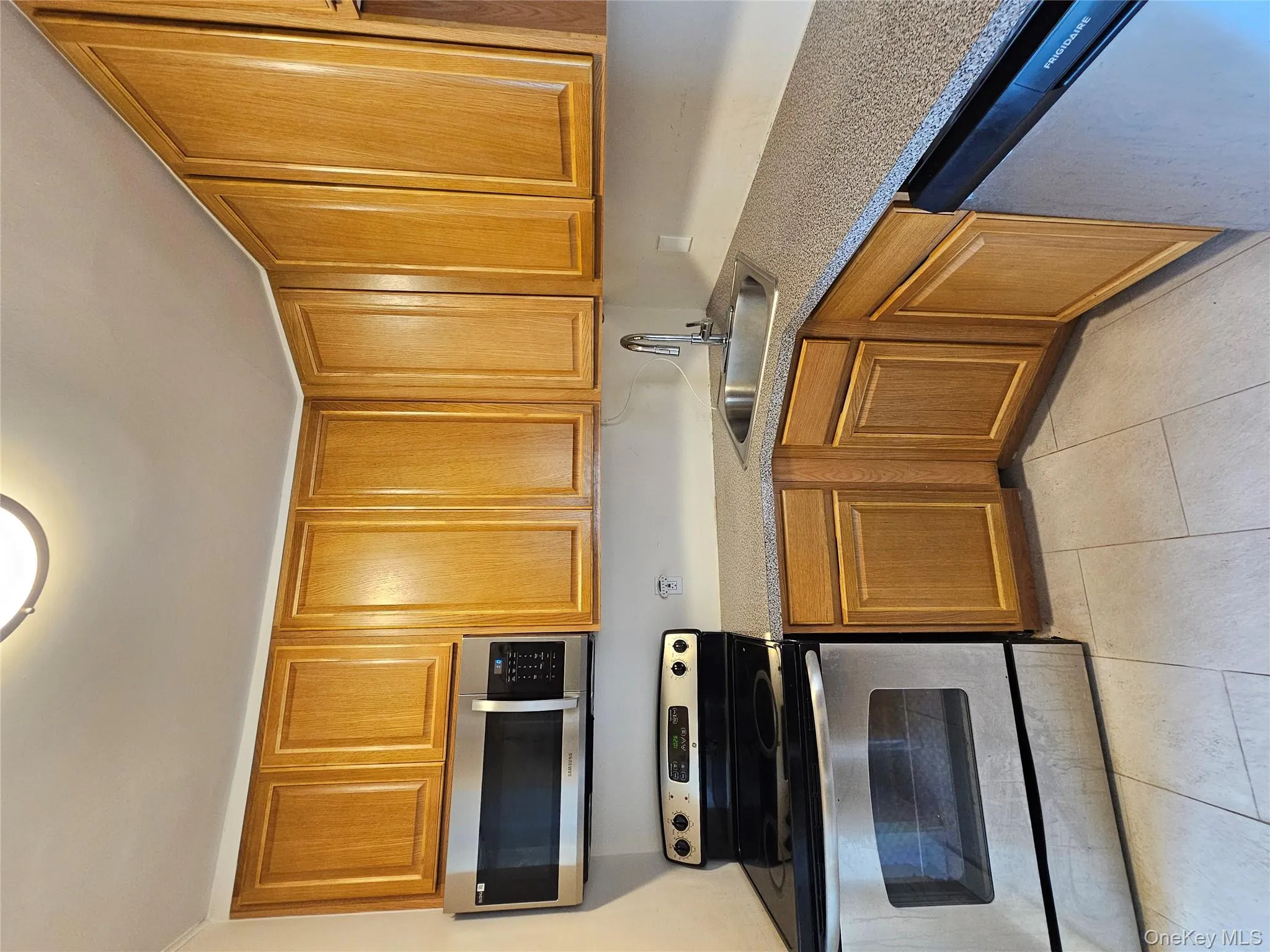 Kitchen featuring stove, stainless steel dishwasher, brown cabinetry, and light tile patterned flooring Kitchen featuring stove, stainless steel dishwasher, brown cabinetry, and light tile patterned flooring