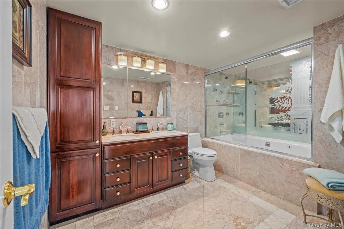 Bathroom featuring elegant tile walls, a double vanity, a tiled shower/tub combo, a Jacuzzi soaking tub, and recessed lighting Bathroom featuring elegant tile walls, a double vanity, a tiled shower/tub combo, a Jacuzzi soaking tub, and recessed lighting