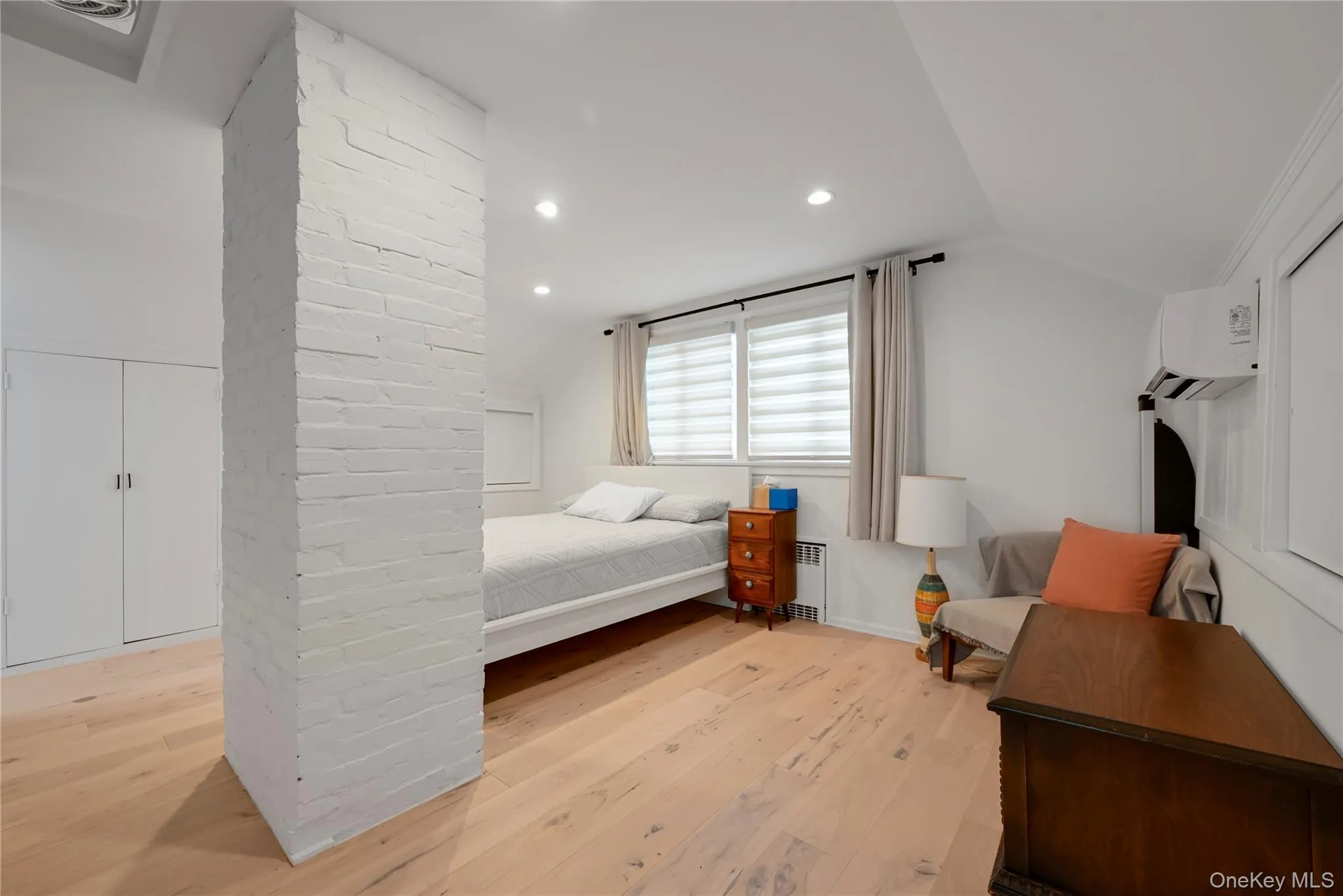 Bedroom with lofted ceiling, light wood finished floors, recessed lighting, radiator heating unit, and a wall mounted AC Bedroom with lofted ceiling, light wood finished floors, recessed lighting, radiator heating unit, and a wall mounted AC