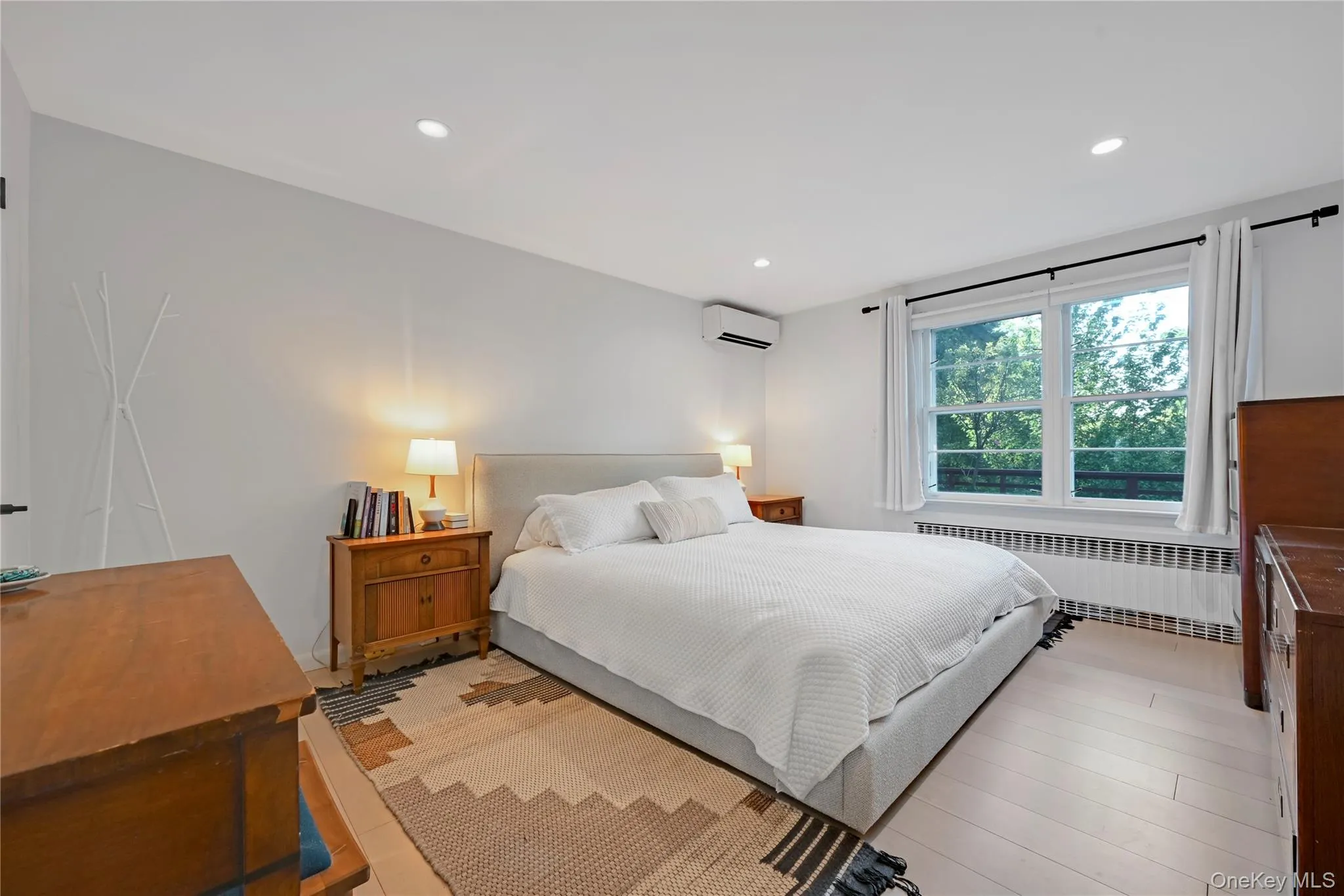 Bedroom with radiator heating unit, light wood finished floors, recessed lighting, and a wall unit AC Bedroom with radiator heating unit, light wood finished floors, recessed lighting, and a wall unit AC