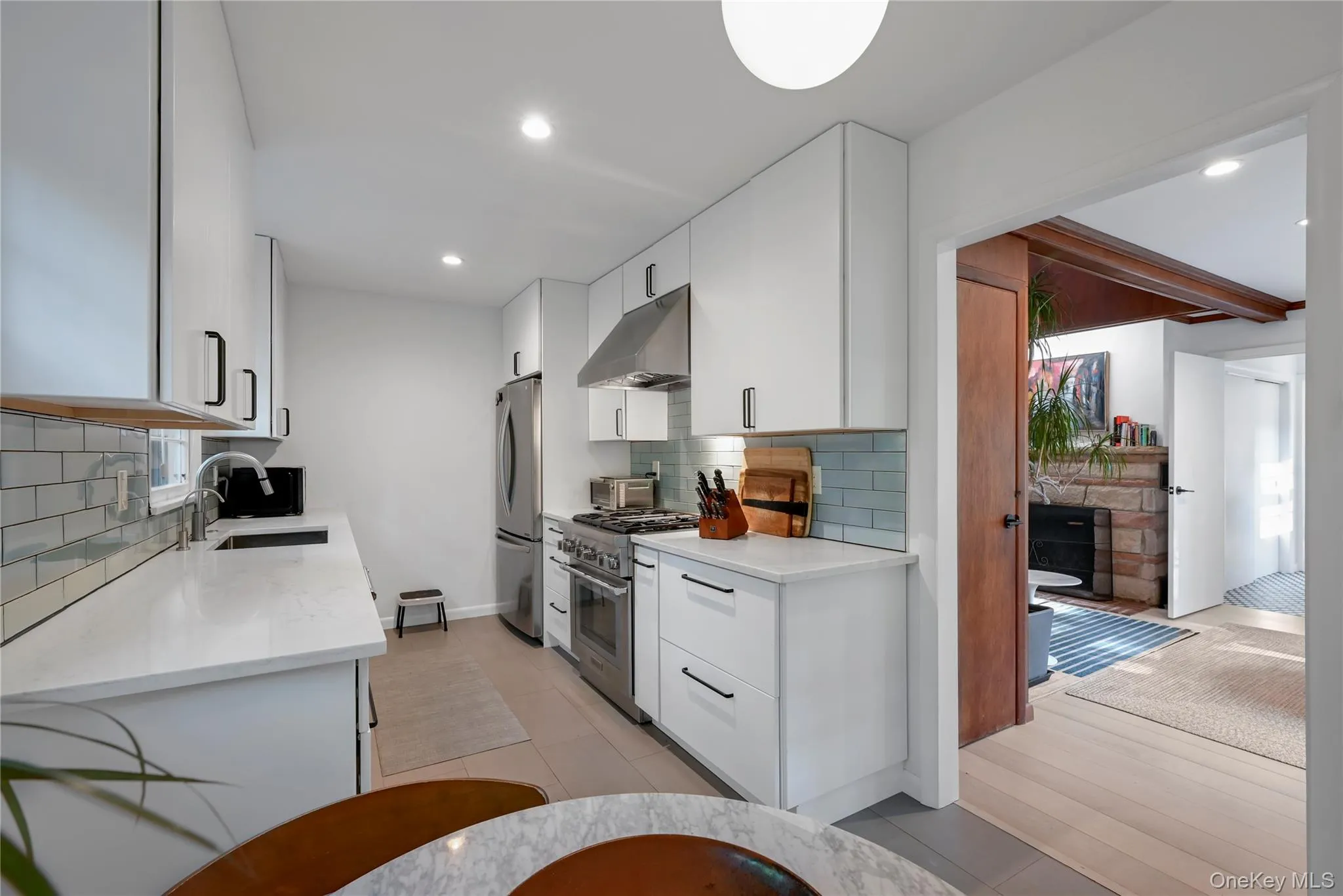 Kitchen featuring tasteful backsplash, white cabinetry, light stone countertops, appliances with stainless steel finishes, and under cabinet range hood Kitchen featuring tasteful backsplash, white cabinetry, light stone countertops, appliances with stainless steel finishes, and under cabinet range hood