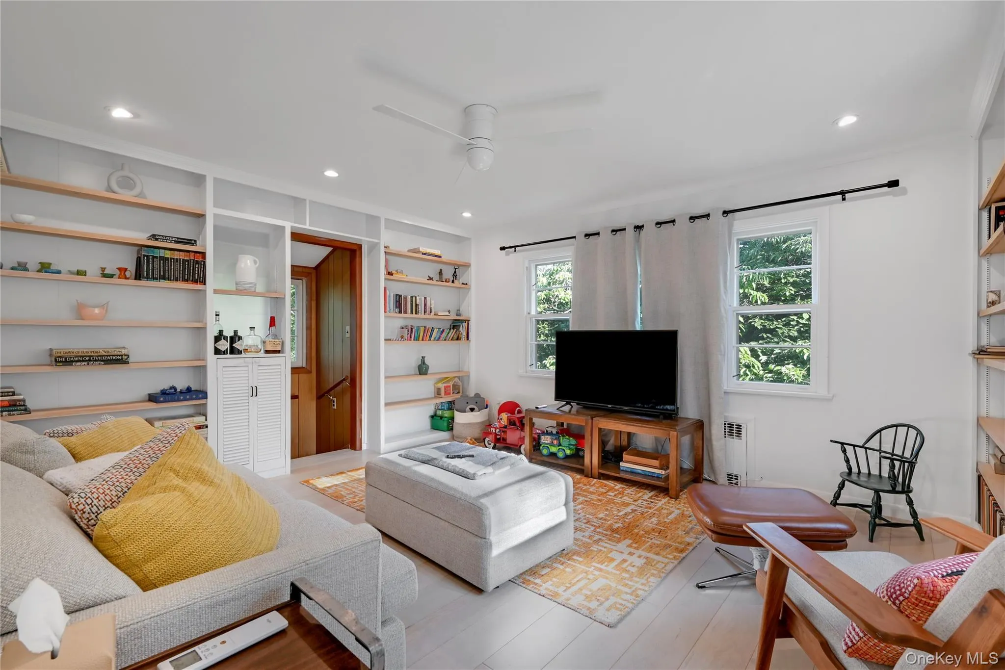 Living room with built in shelves, ceiling fan, recessed lighting, wood finished floors, and radiator Living room with built in shelves, ceiling fan, recessed lighting, wood finished floors, and radiator