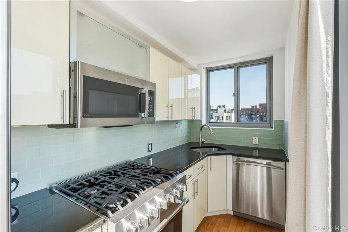 Kitchen with appliances with stainless steel finishes, tasteful backsplash, white cabinetry, light wood-style flooring, and dark stone counters Kitchen with appliances with stainless steel finishes, tasteful backsplash, white cabinetry, light wood-style flooring, and dark stone counters