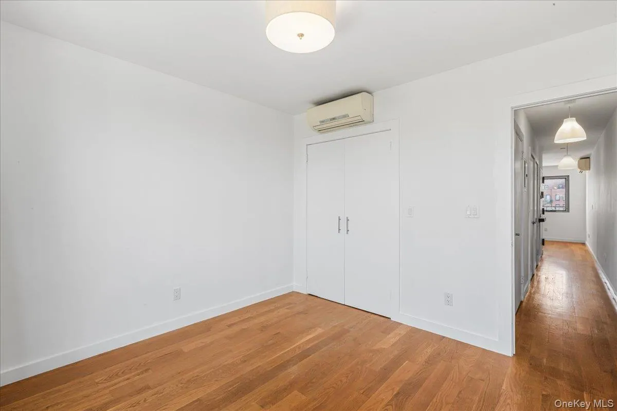 Unfurnished bedroom with light wood-style flooring, a closet, and an AC wall unit Unfurnished bedroom with light wood-style flooring, a closet, and an AC wall unit