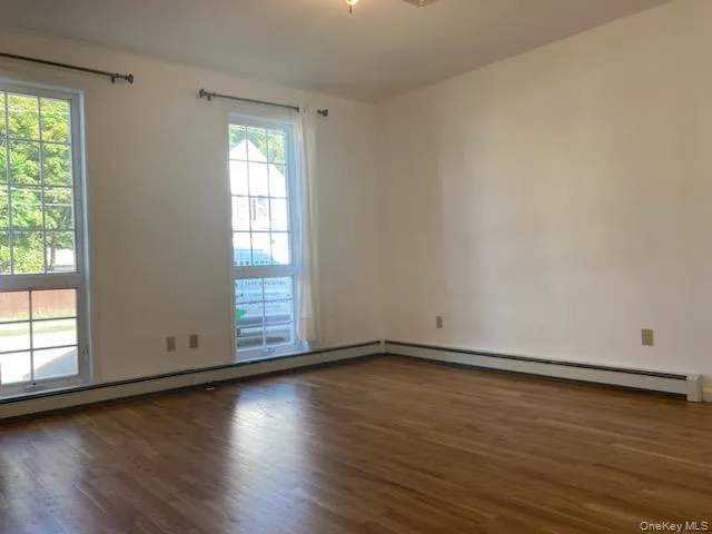 Empty room featuring dark wood-style floors, a baseboard radiator, and baseboard heating Empty room featuring dark wood-style floors, a baseboard radiator, and baseboard heating